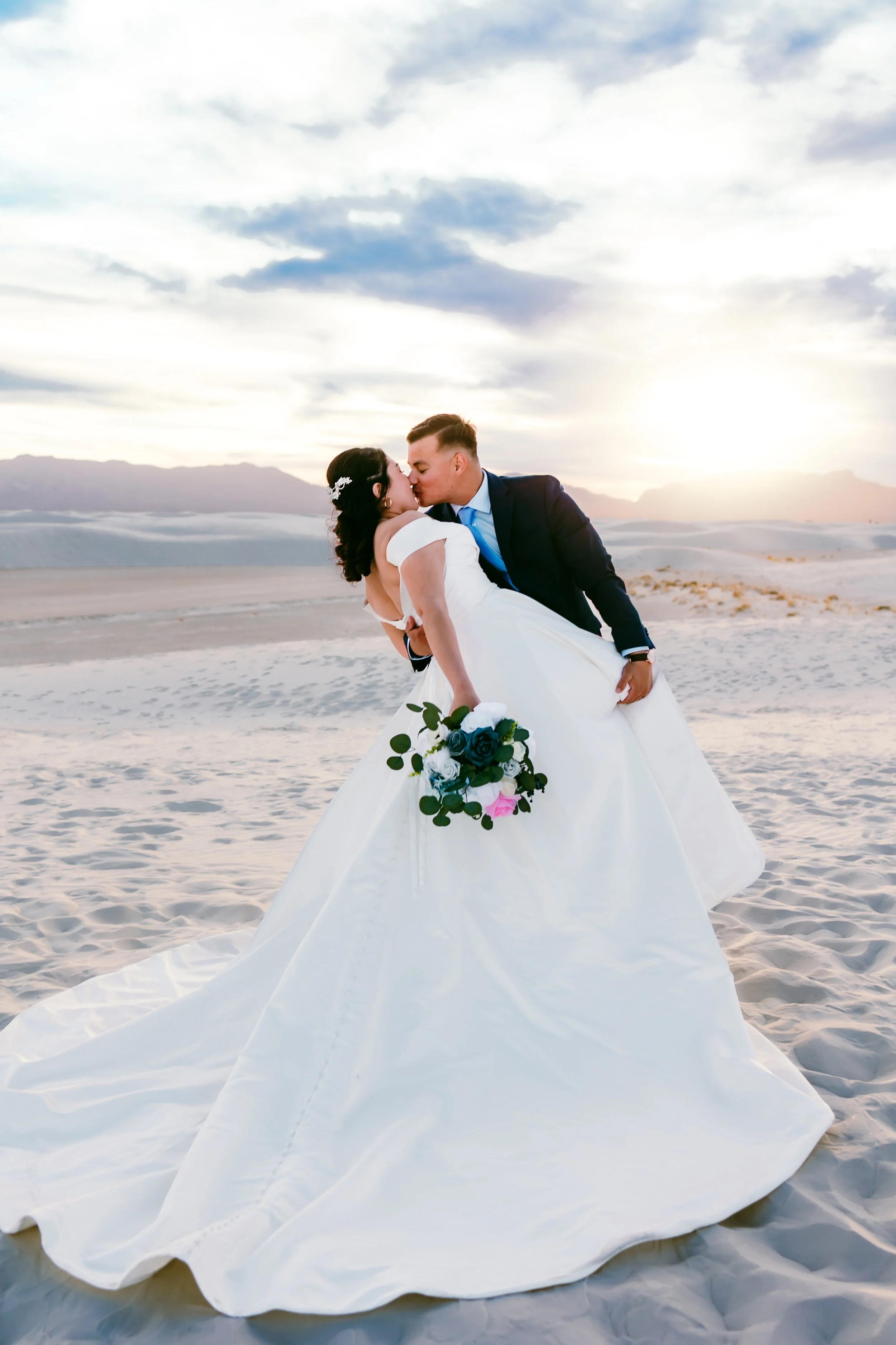 Bride and groom sharing a romantic dip kiss at sunset among the white dunes of White Sands National Park in New Mexico.