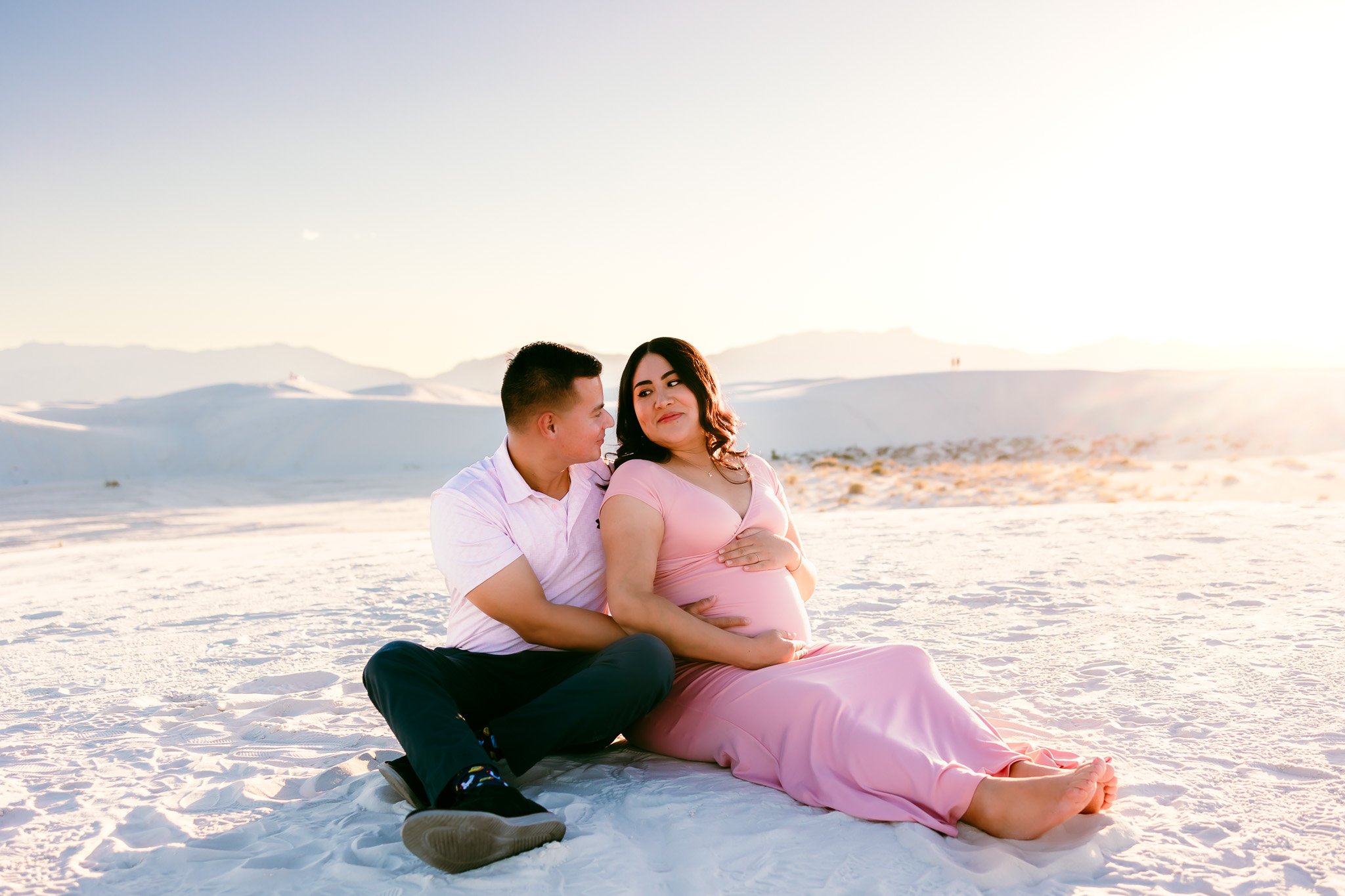 Couple sitting together on the white sand dunes during a maternity photography session at White Sands National Park, New Mexico.