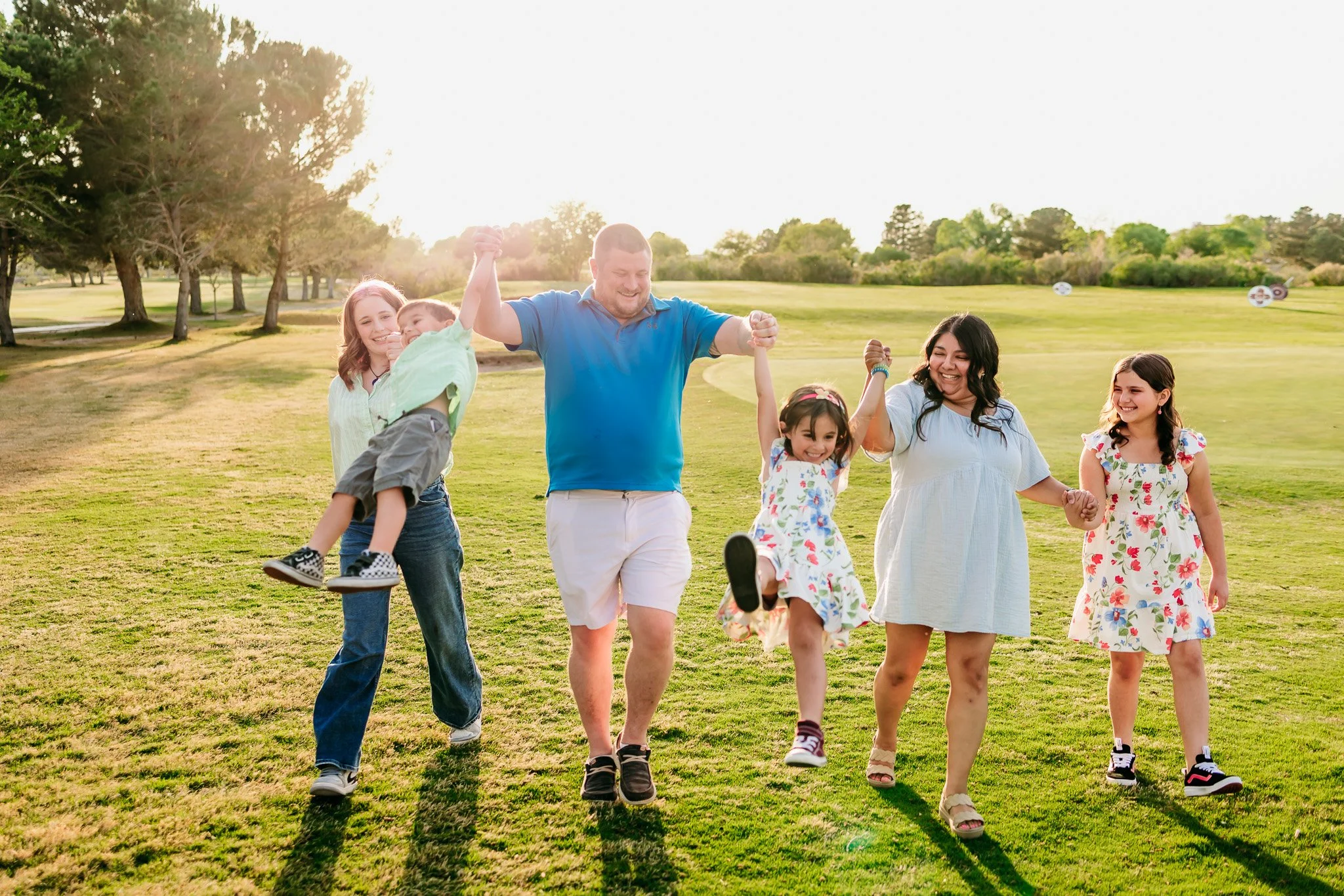 Parents walking hand in hand with their children during a golden hour family session at NMSU Golf Course in Las Cruces, New Mexico.