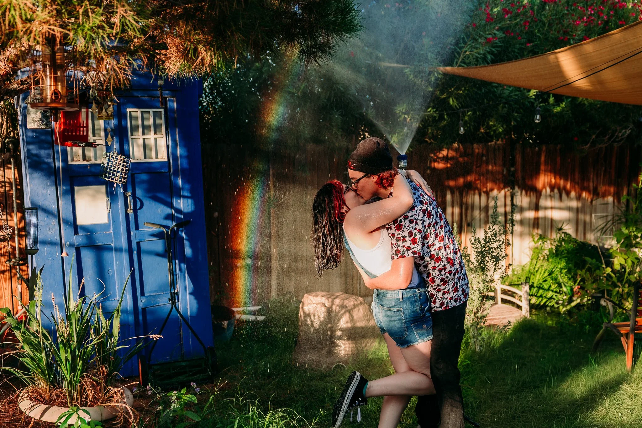 Couple sharing a romantic embrace in a lush backyard garden during a lifestyle couples session at their home in Las Cruces, New Mexico.