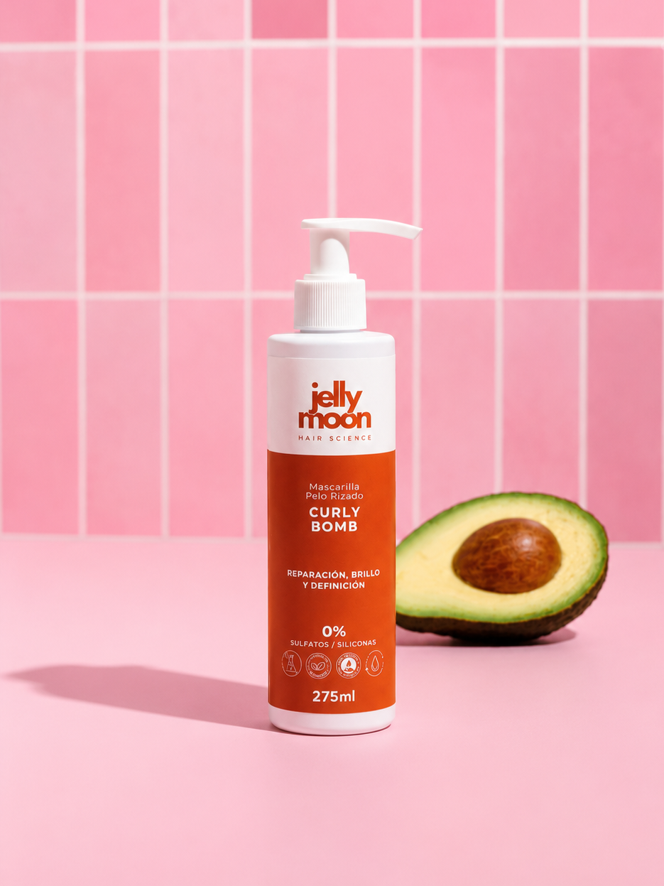 Botella de mascarilla para cabello rizado 'Jelly Moon' en un fondo rosa con medio aguacate al lado