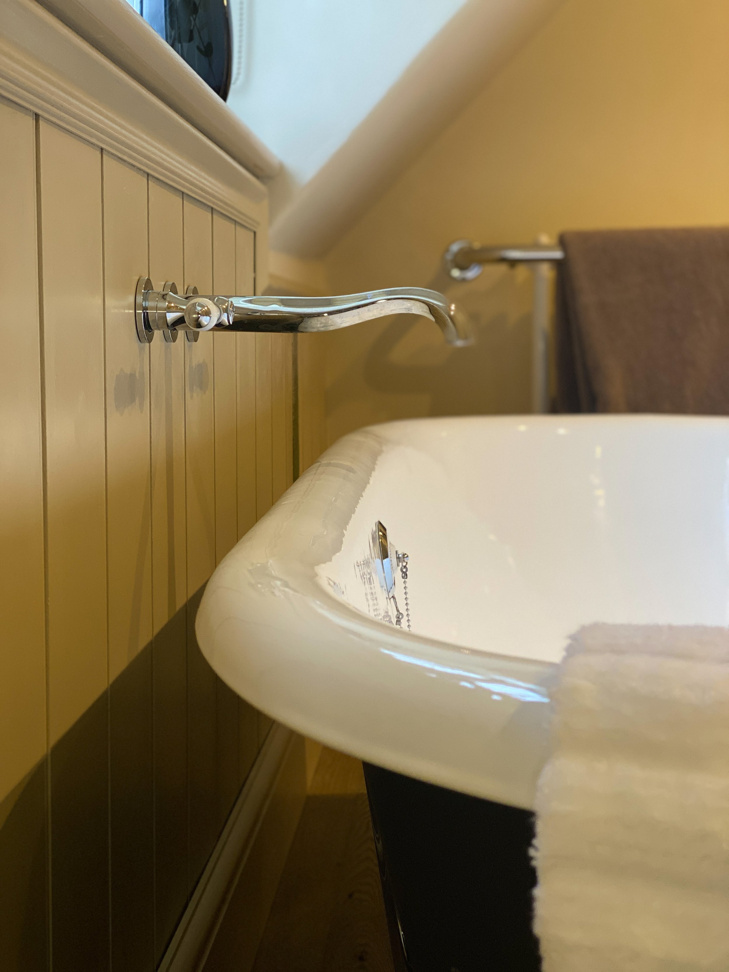Close-up of a vintage-style chrome faucet mounted on a bathroom sink with a wooden cabinet and a mirror in the background.