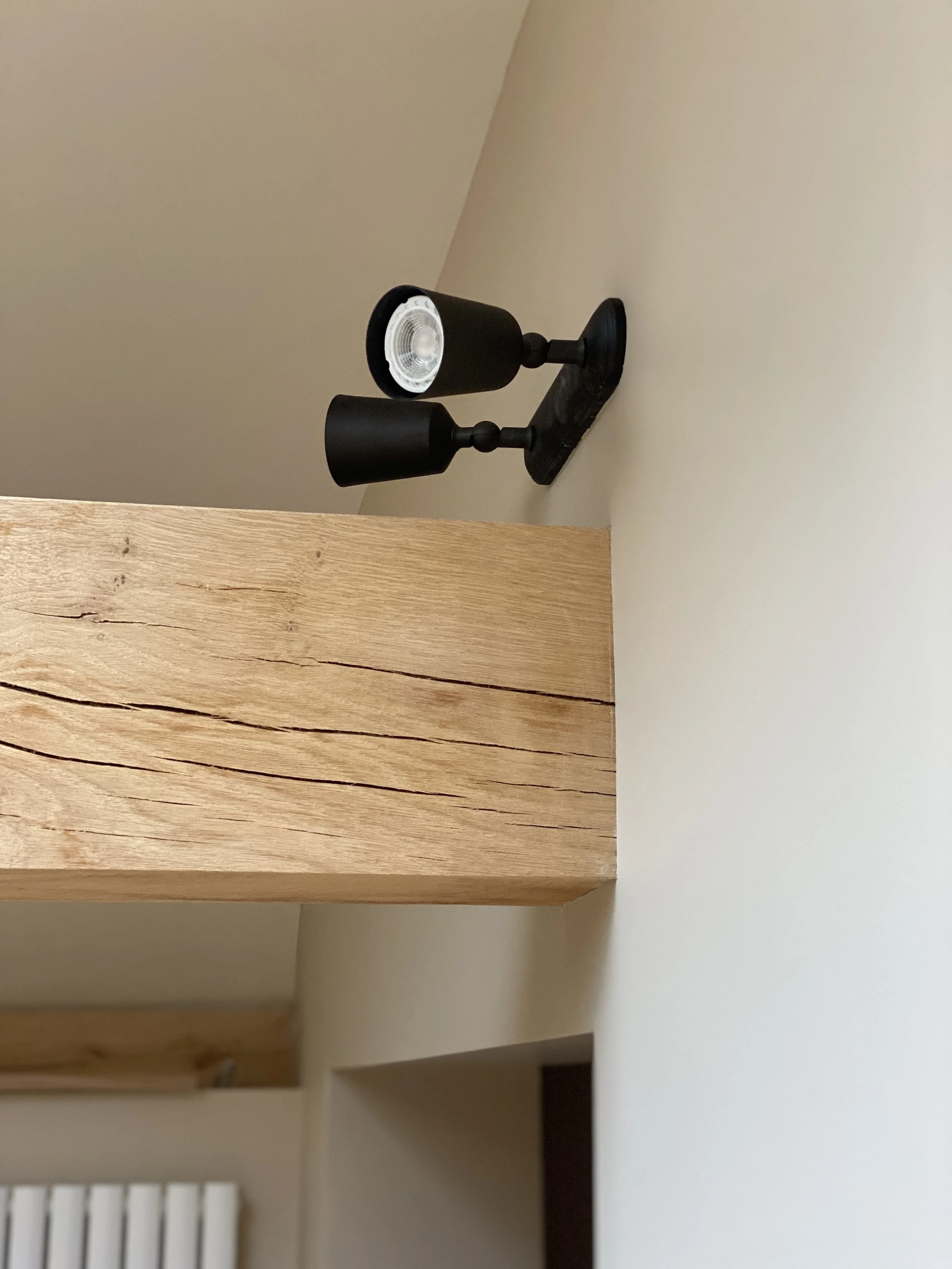 Black adjustable spotlight lamp mounted on a wooden beam and white wall.