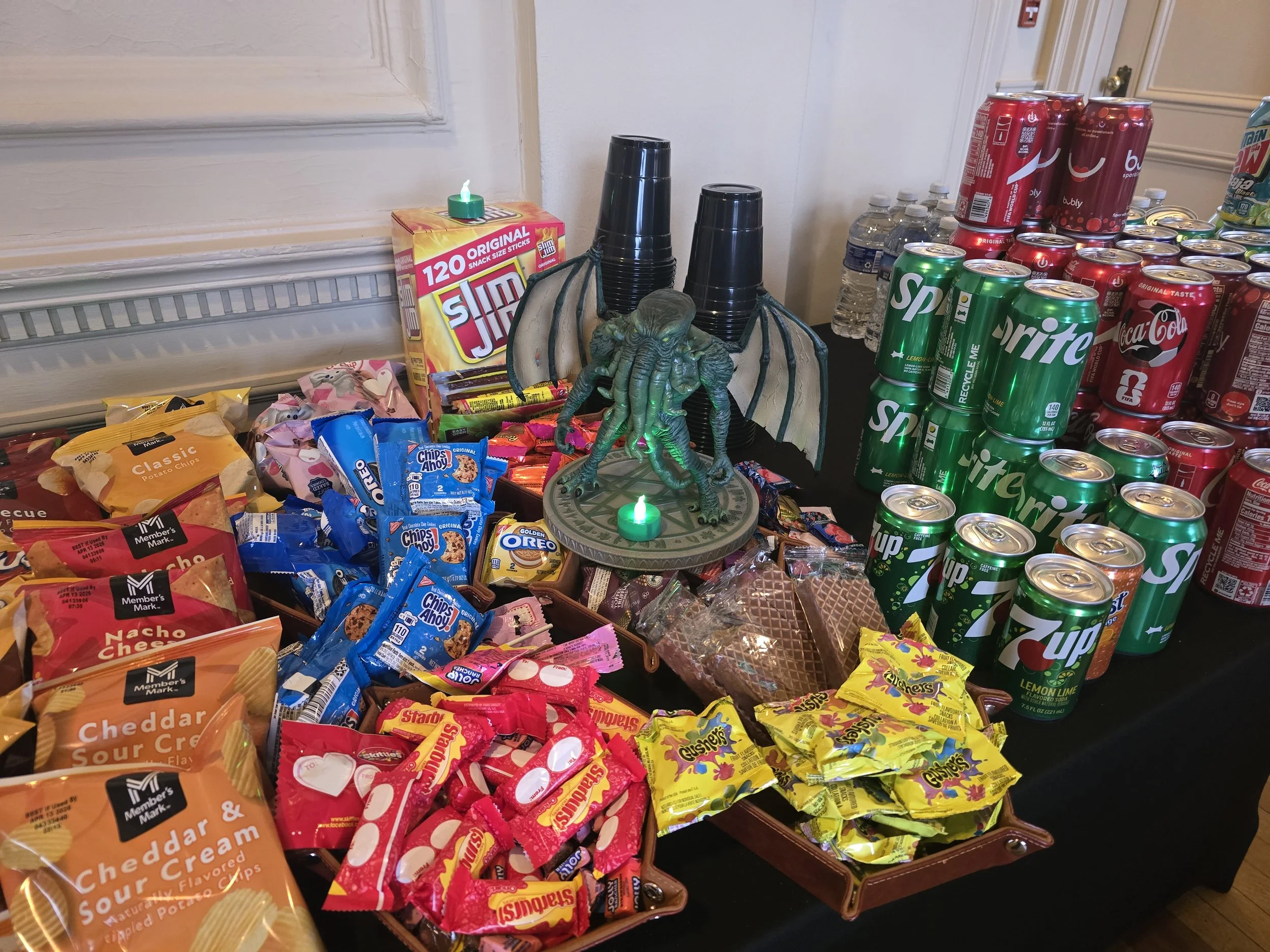 Buffet table with water bottles, soda cans, and snacks in a stone hall decorated with paintings, sculptures, and set up for a gathering or event.