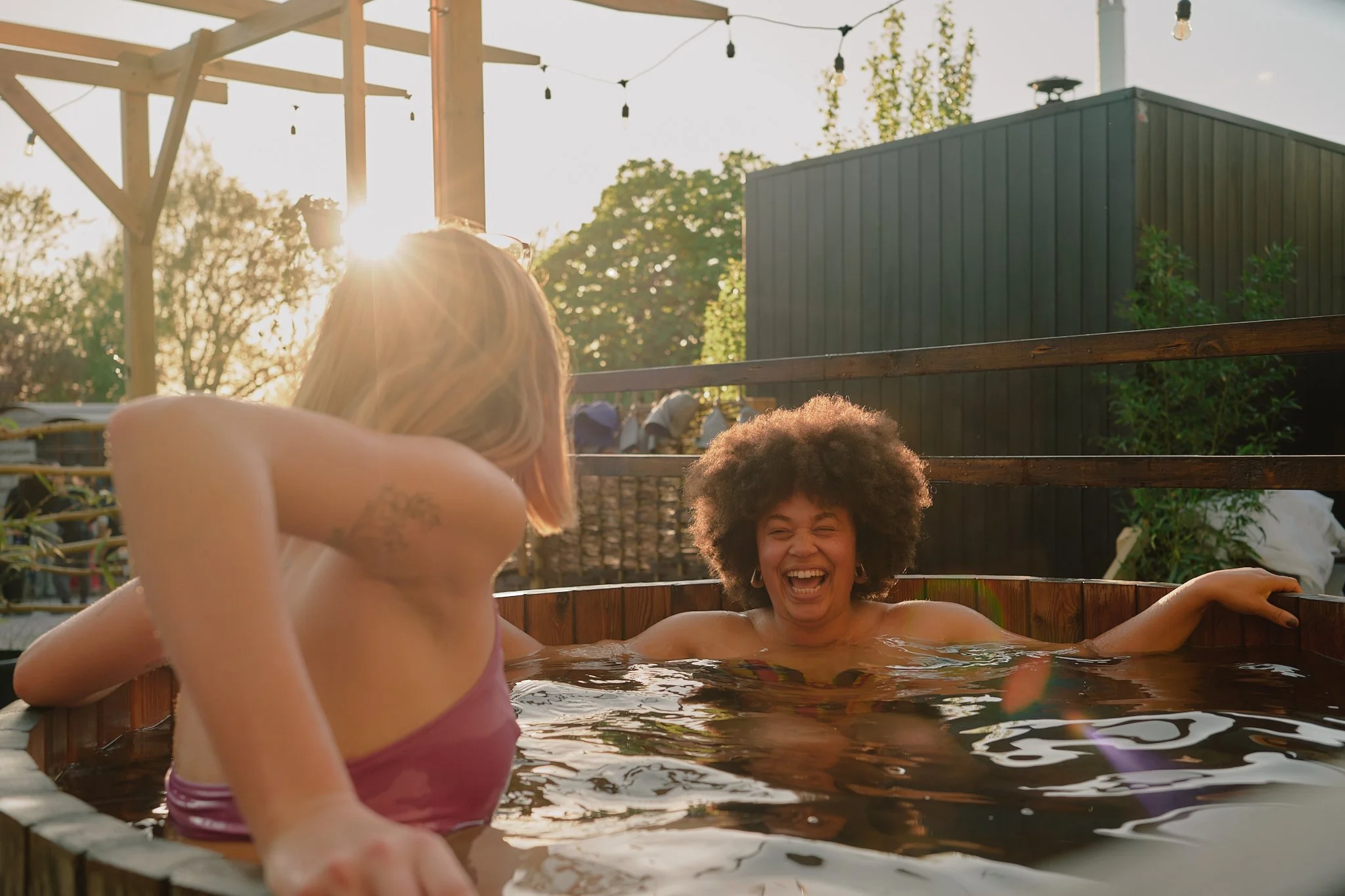 Two women enjoying a hot tub outdoors during sunset, smiling and laughing.