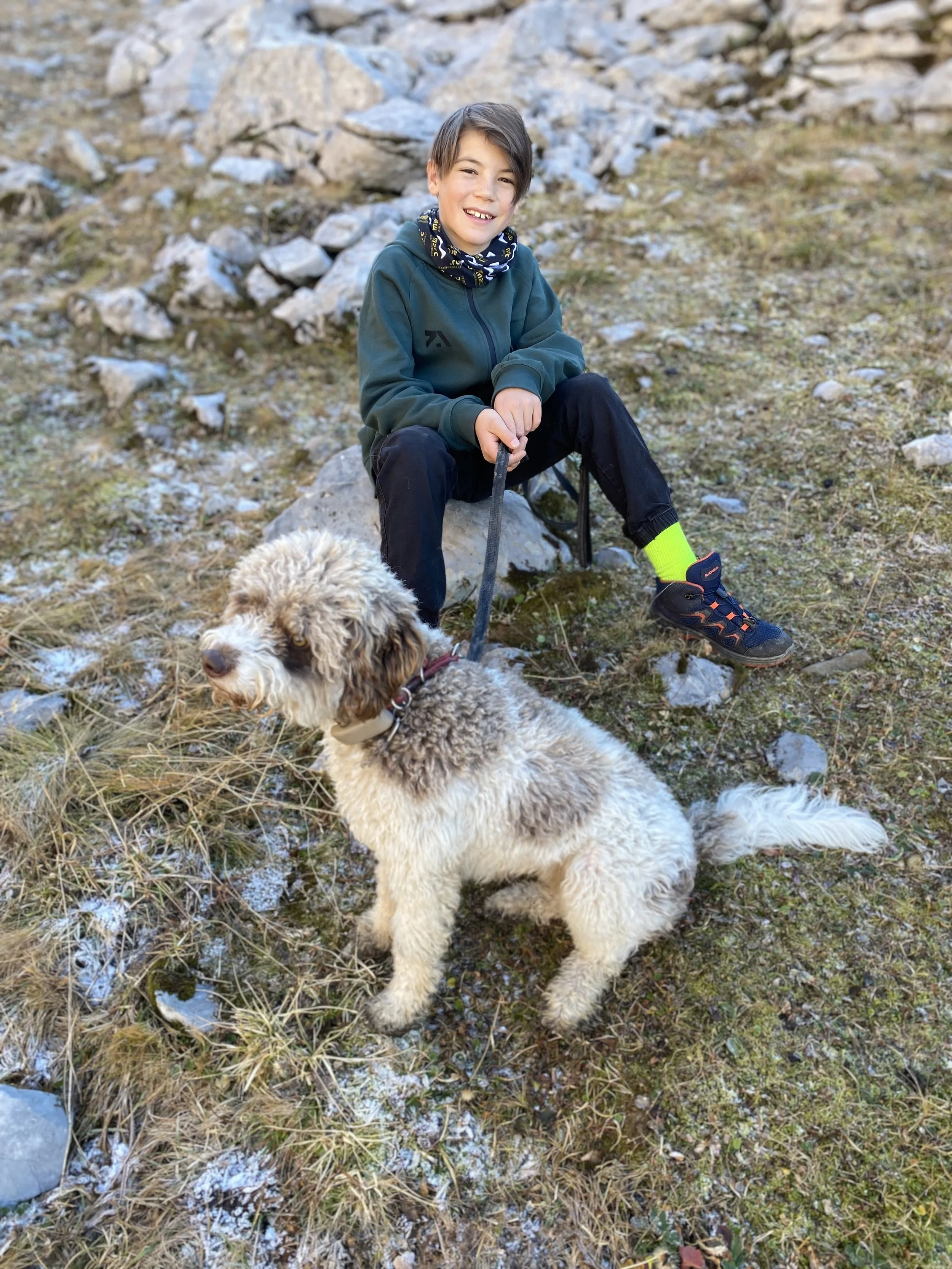 Ein Junge mit einem Hund im Freien auf einer felsigen und bewachsenen Landschaft