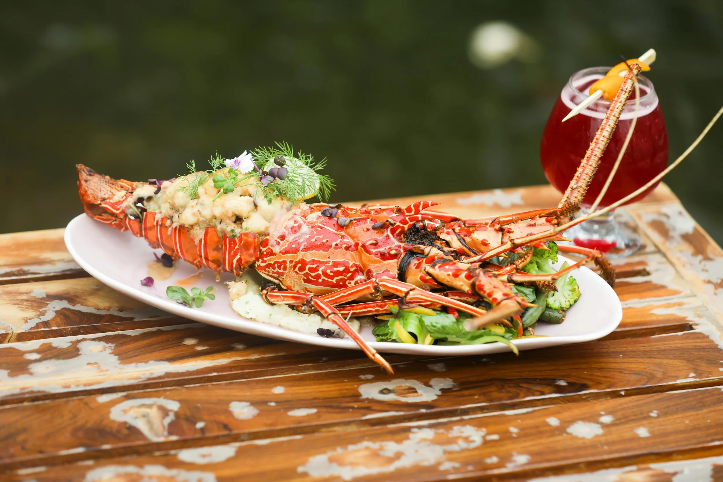 Homard ou langouste cuisiné avec une salade et une boisson rouge sur une table en bois