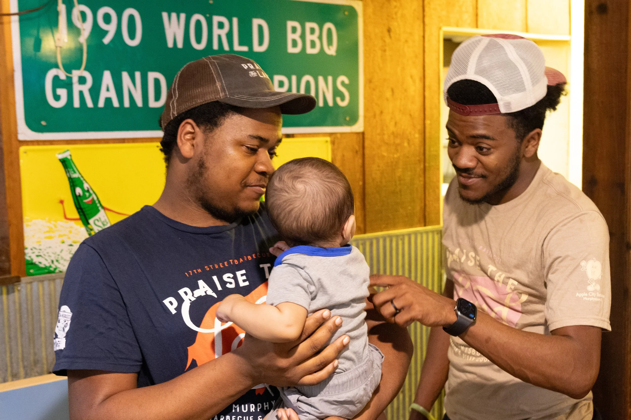 At the end of his shift, Kitchen Manager Jakaylen Myers holds his baby Simeon alongside his brother Savior inside 17th Street Barbecue