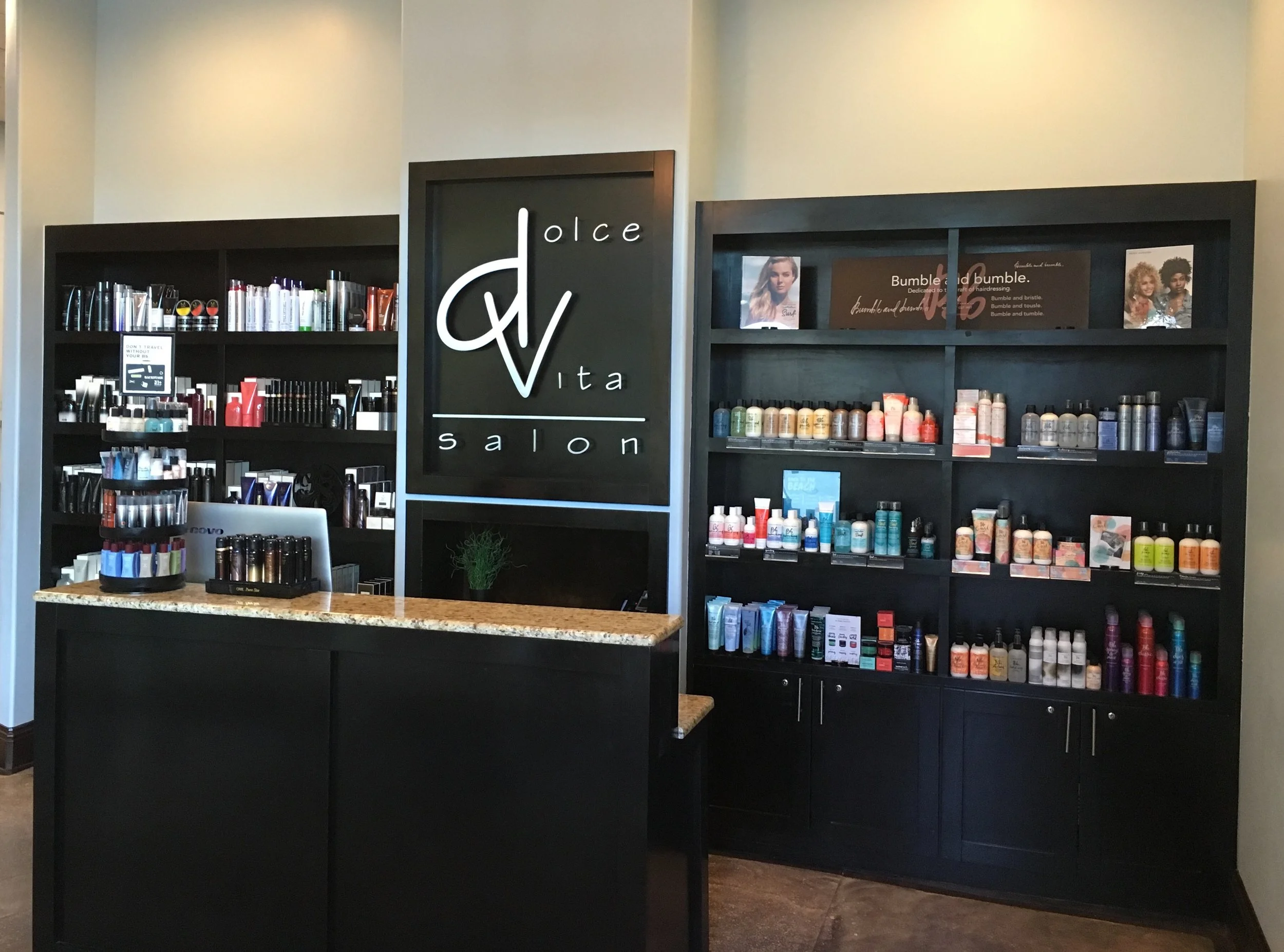 Interior view of a salon with shelves of hair and beauty products, a sign with the salon's name 'Dolce Vita Salon', and a black countertop in the foreground.