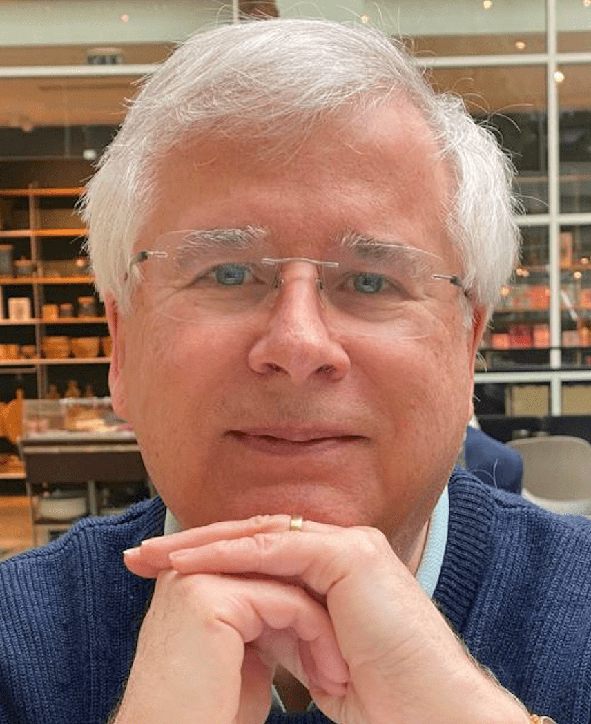 Photo of man with white hair and glasses smiling resting his chin on his hands