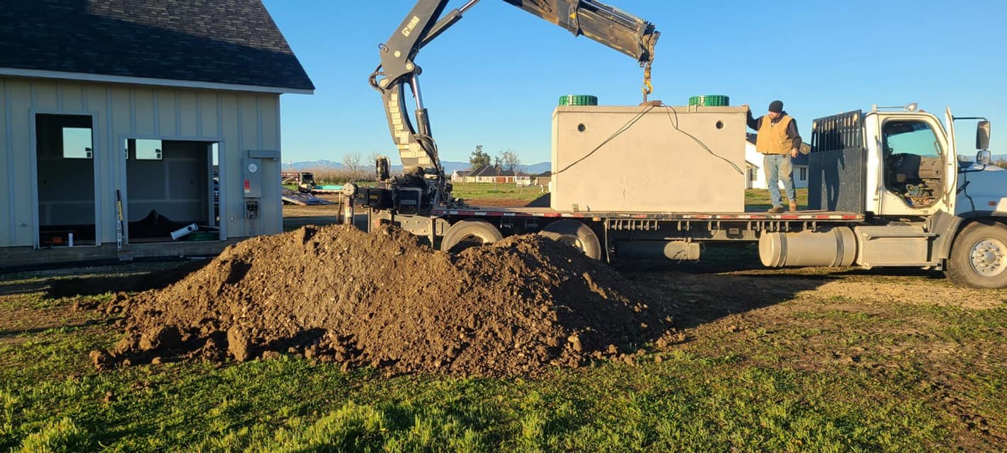 A Robert Burt Construction site with a flatbed truck, a large pile of dirt, a concrete block, and a worker in a black hat standing on the truck.