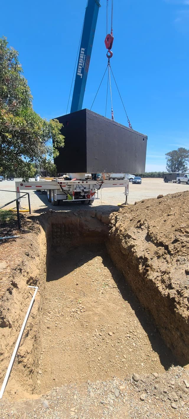 A large black block being lifted by a crane above a construction excavation site by Robert Burt Construction with dirt walls on either side.
