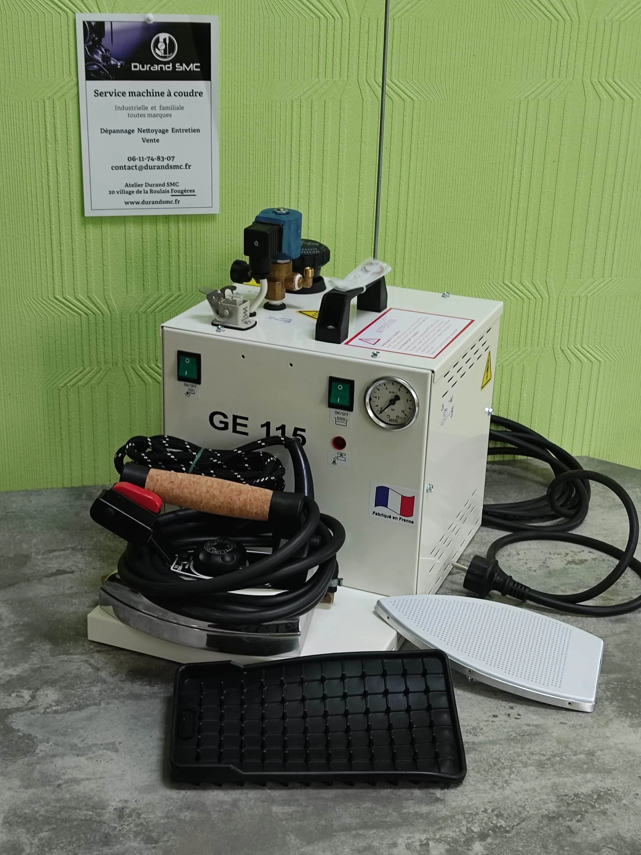 Machine à coudre avec accessoires, câbles, panier en plastique, et panneau d'information en français contre un mur vert.