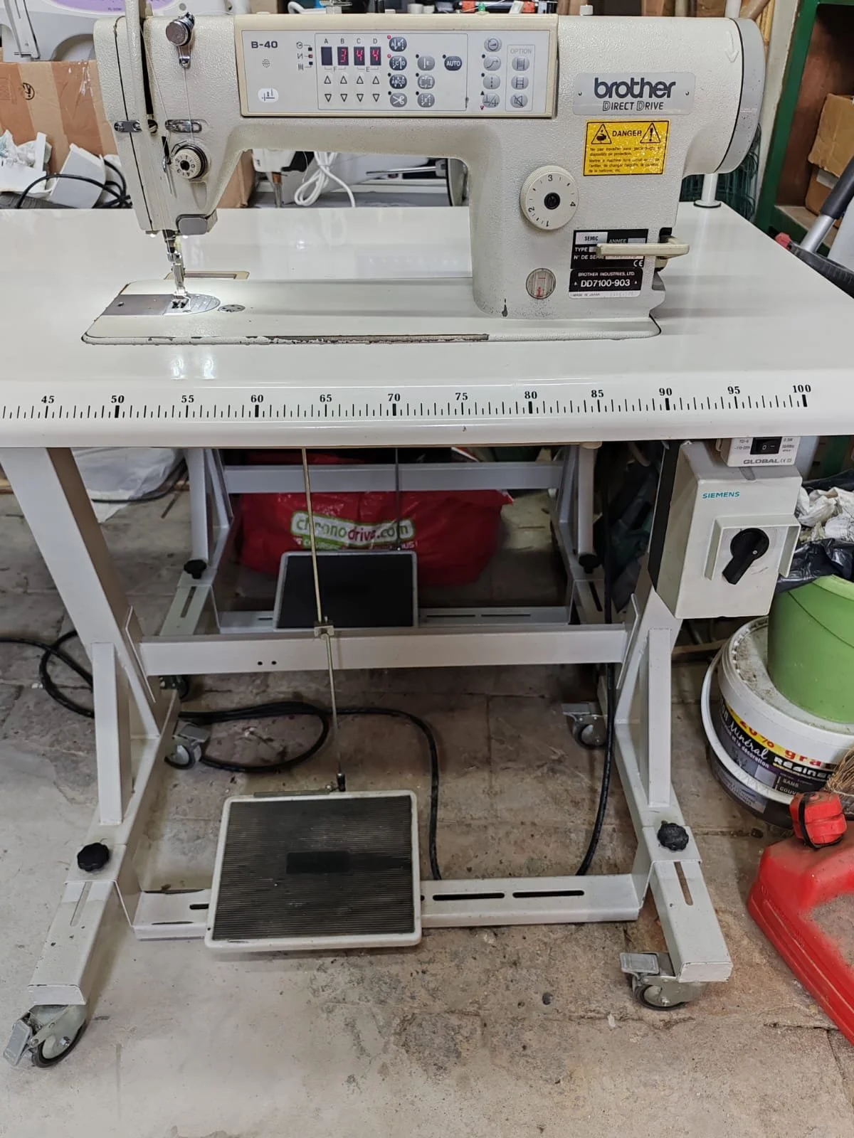 Machine à coudre Brother sur un bureau blanc avec roulettes, dans un atelier, avec diverses fournitures autour.