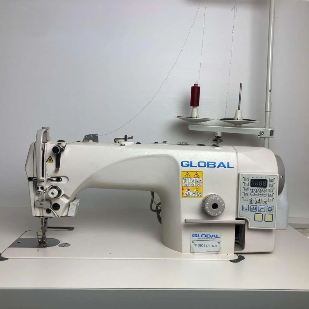 Machine à coudre industrielle blanche avec le logo 'GLOBAL' et un panneau de contrôle numérique sur le côté droit, située en salle blanche avec des fils à l'arrière.