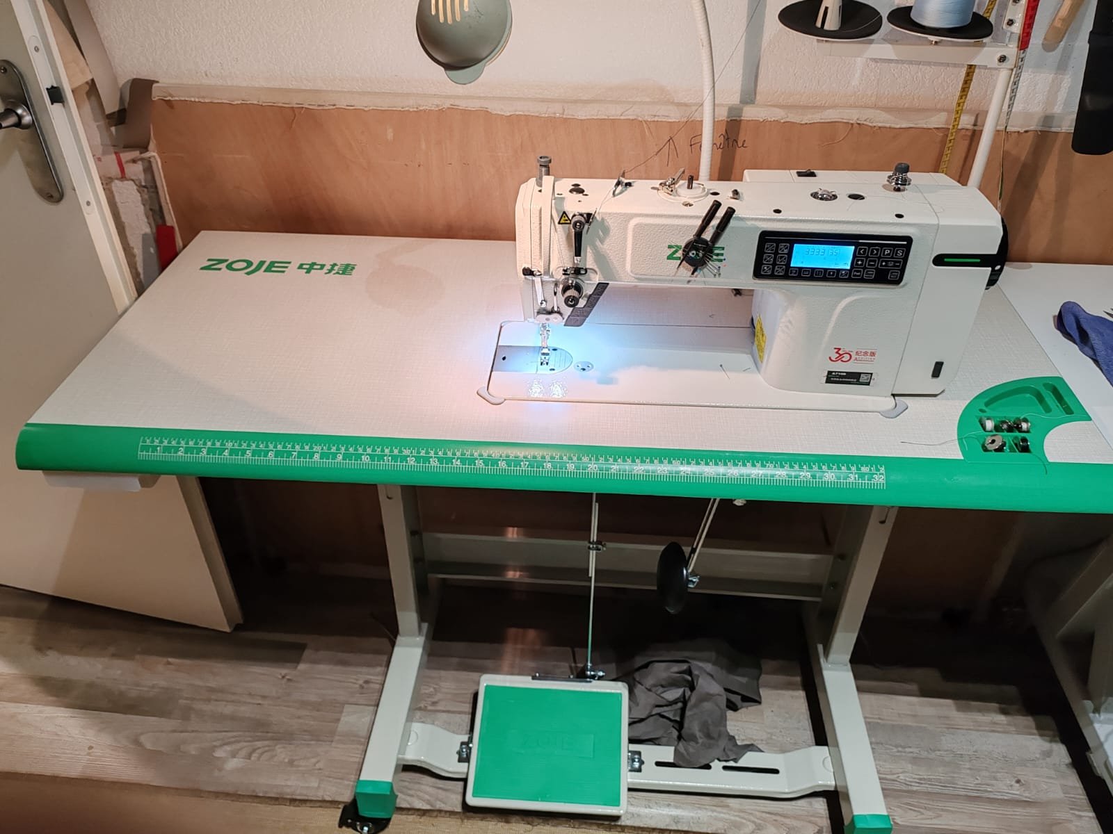 Machine à coudre industrielle sur une table de couture avec une règle verte intégrée au bord, située dans un atelier.