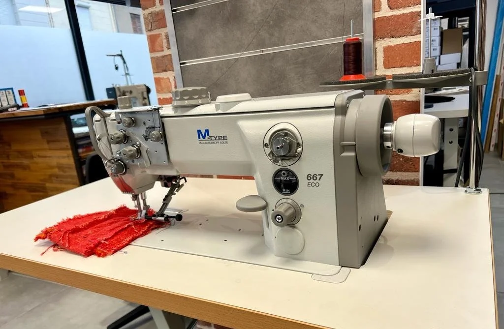 Une machine à coudre industrielle avec un morceau de tissu rouge sous la aiguille, dans un atelier de couture.