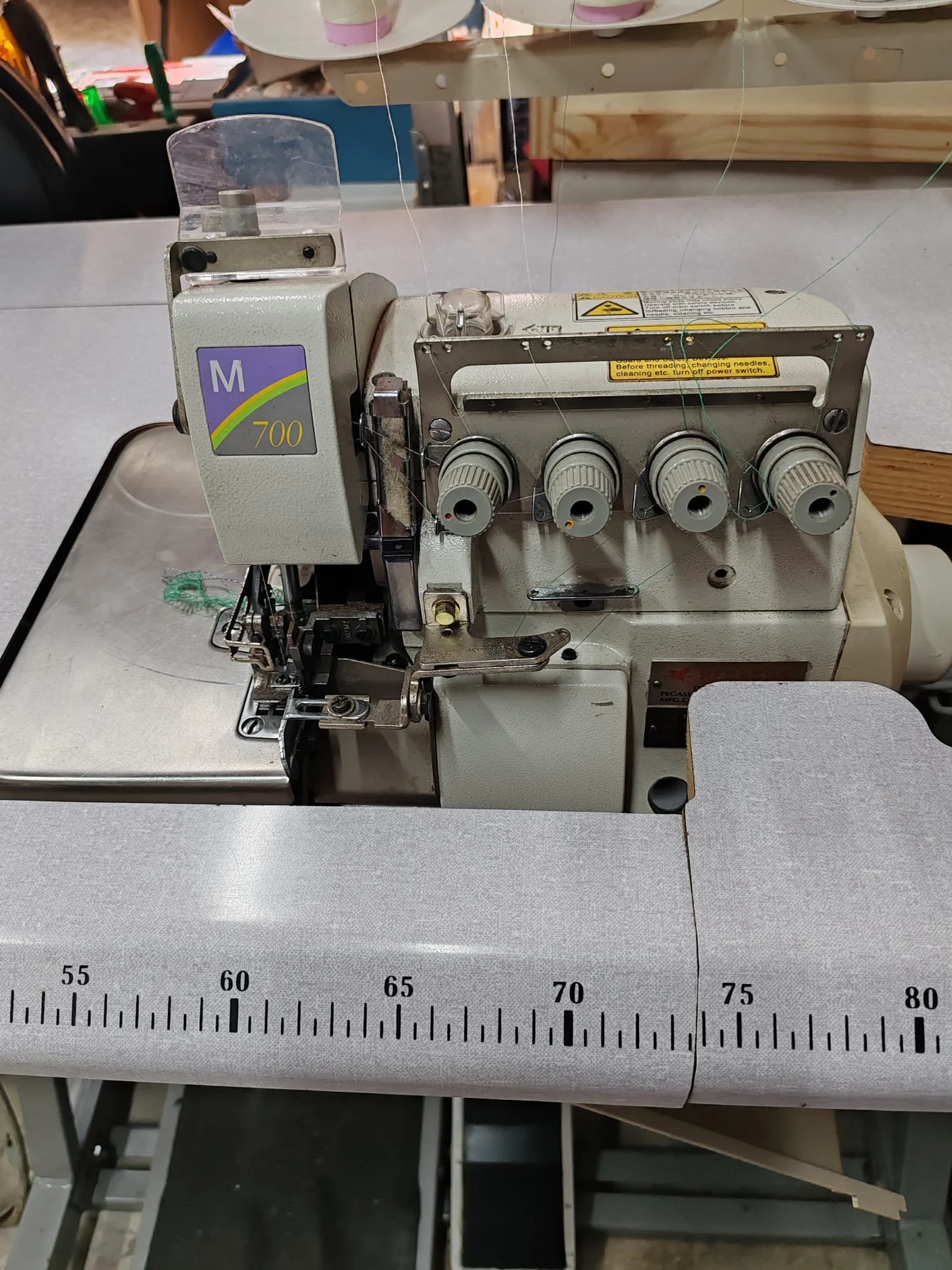 Machine à coudre industrielle avec réglages pour la couture, sur un bureau de tailoring avec une règle de mesure en centimètres au premier plan.