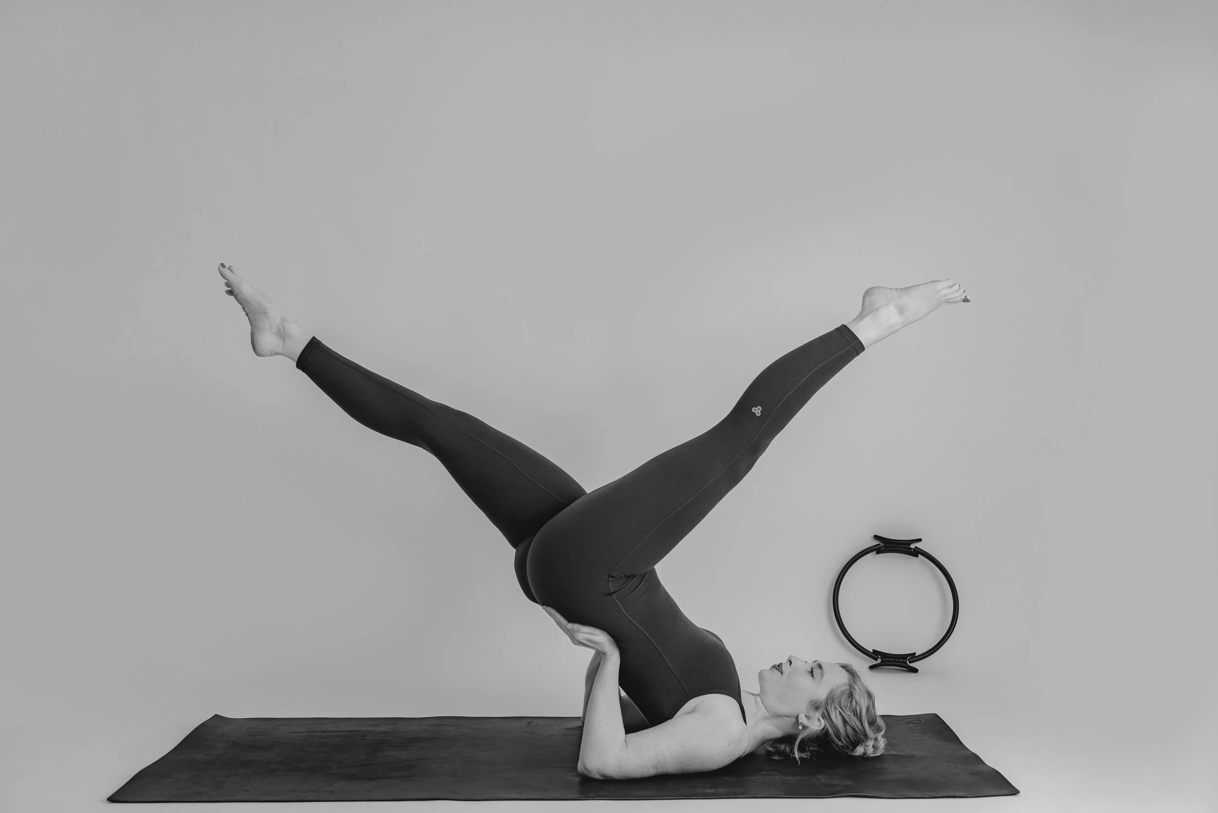 Woman practicing Pilates on a mat, lying on her back with legs raised and spread apart in a Pilates pose called High Scissors.