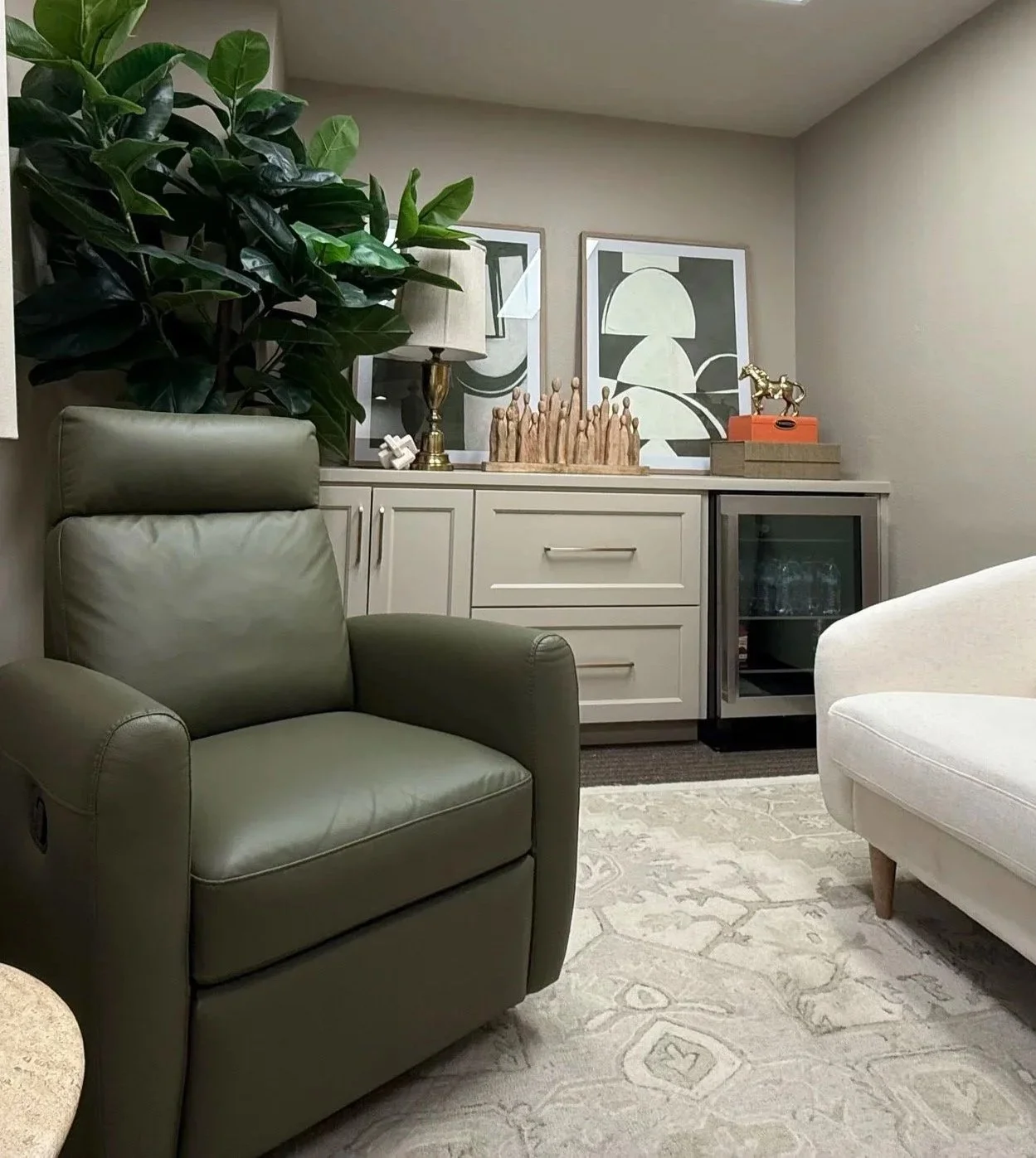 Living room with a beige sideboard decor with two framed black and white abstract art pieces, a large green plant, a brass lamp, a piece of modern wooden art, a small gold horse sculpture, and a small orange box on top.