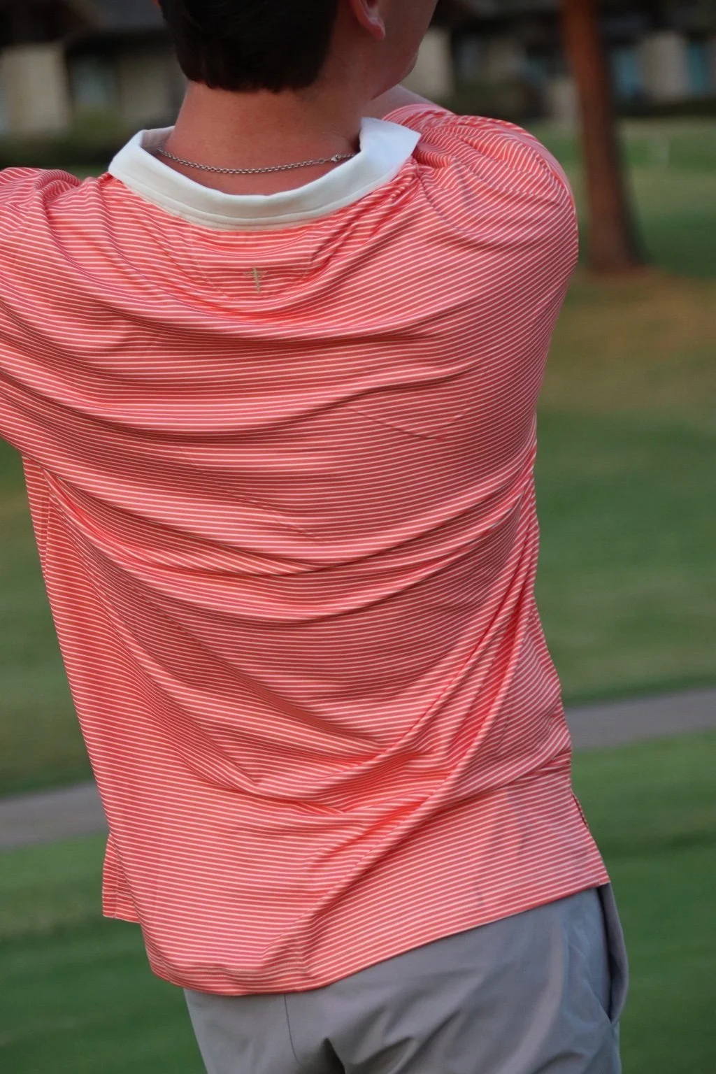 Back view of a golfer in The Striped Classic polo in coral with a white collar