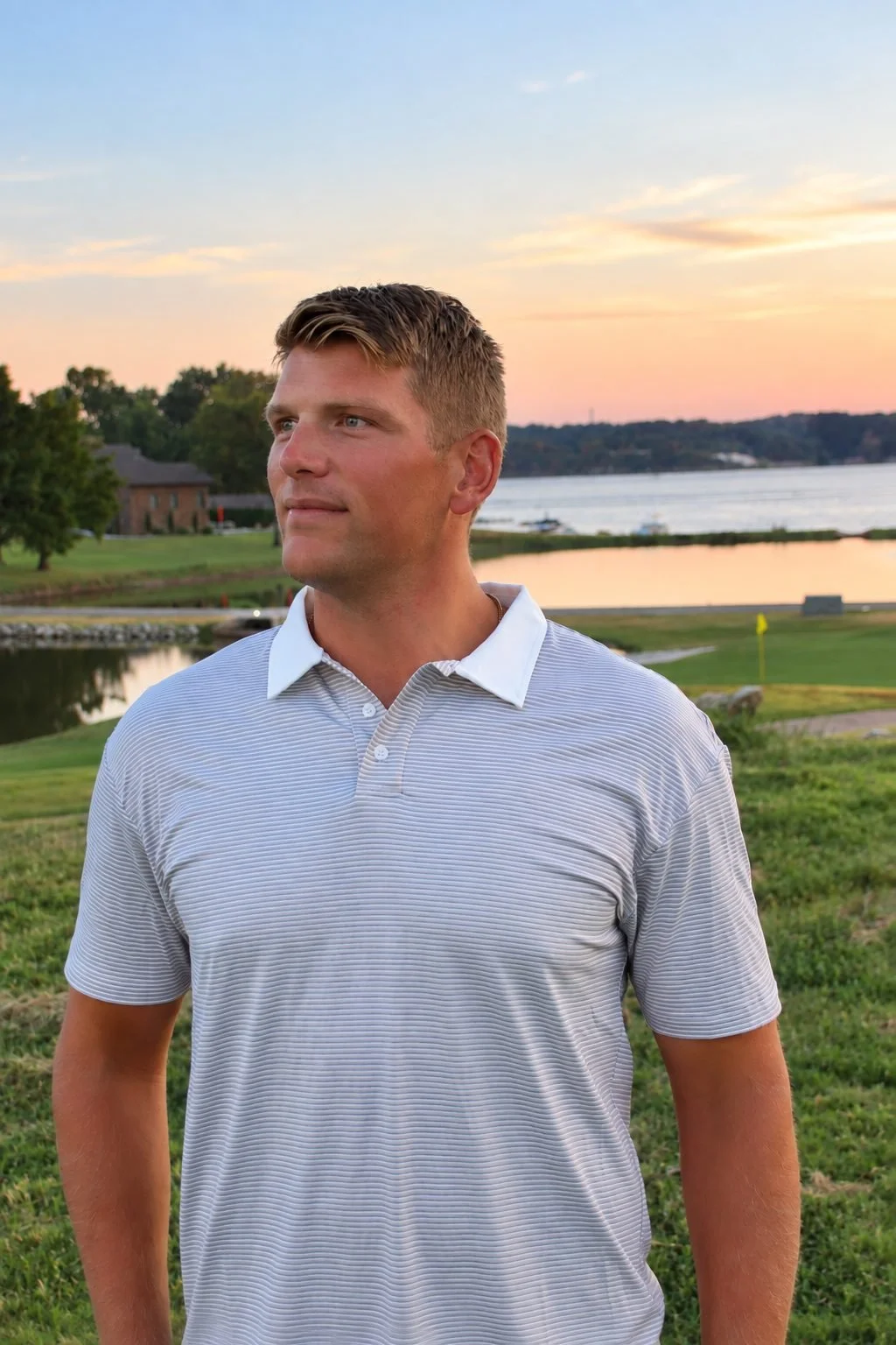 Man wearing The Striped Classic polo in gray with a white collar on a golf course at sunset
