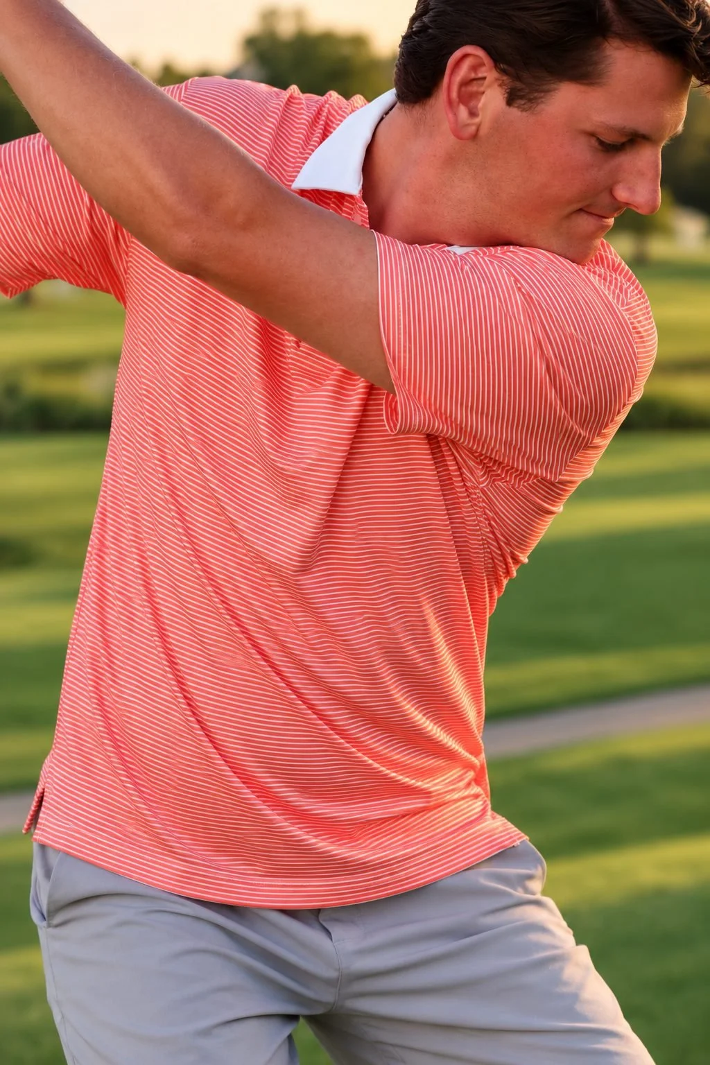 Man mid golf swing wearing The Striped Classic polo in coral