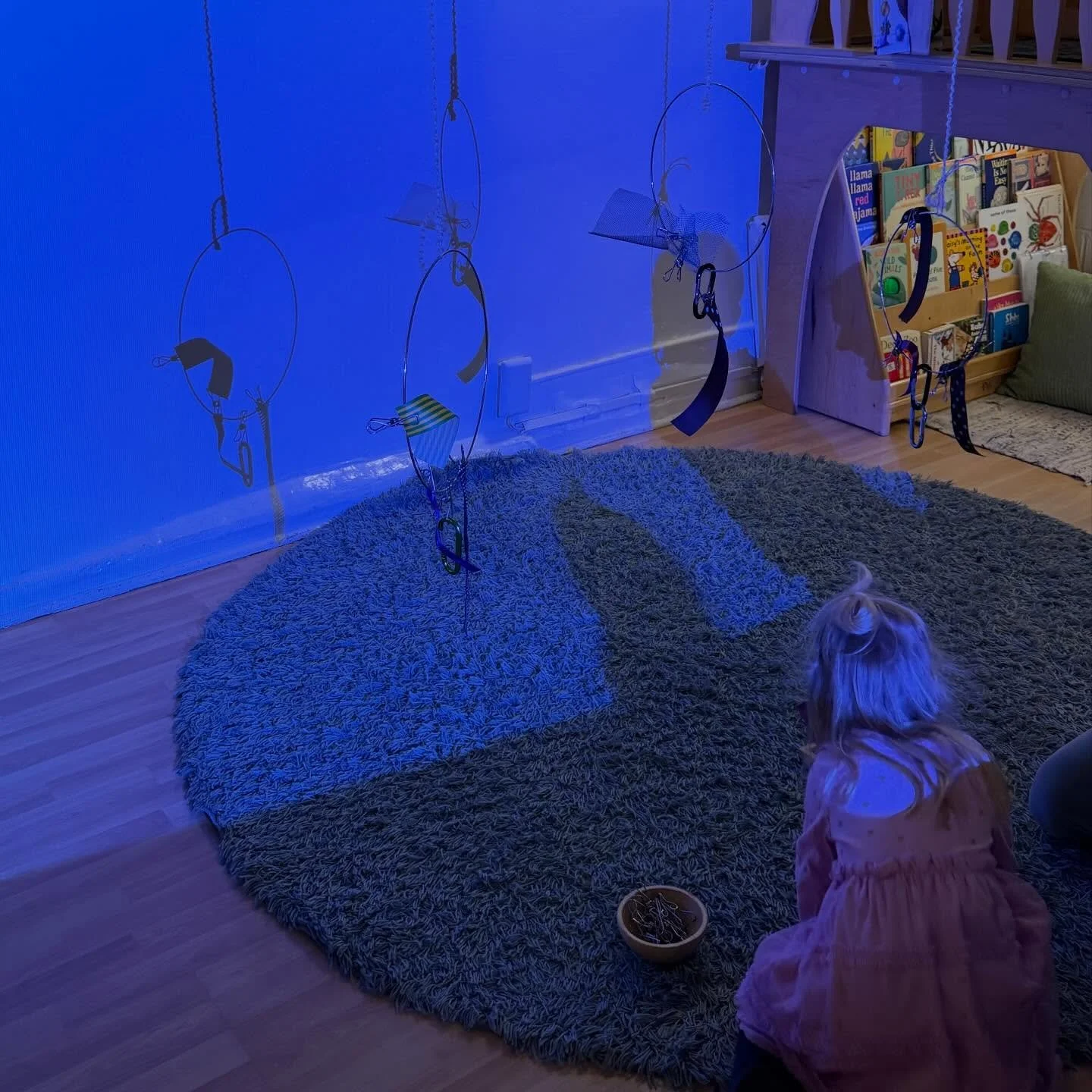 In the toddler room, large hoops were suspended along with ribbons and clips and a projector to cast their shadows onto the wall. While some children were interested in the fine motor challenge of attaching the clips and ribbons, others experimented 