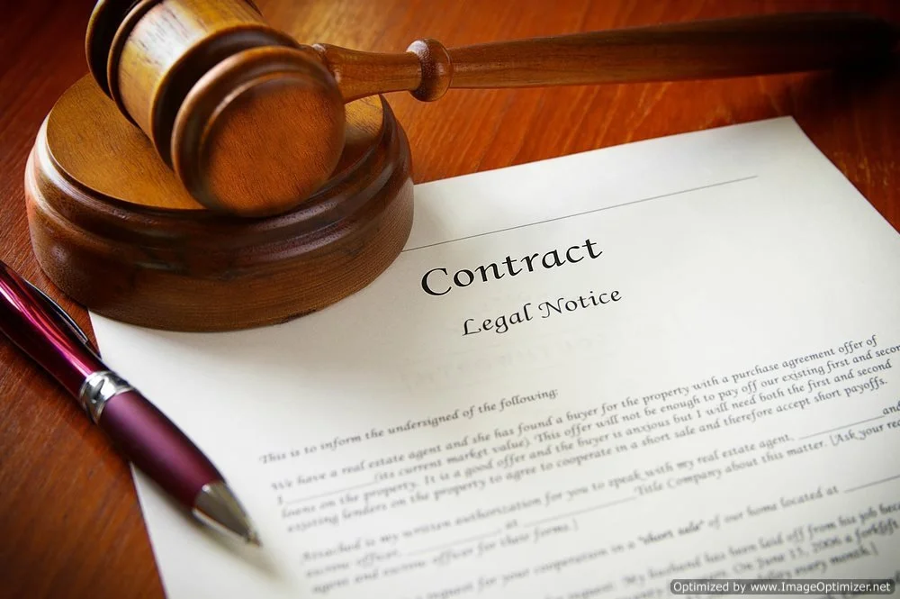 A wooden gavel resting on a legal document titled 'Contract' with a pen lying beside it.