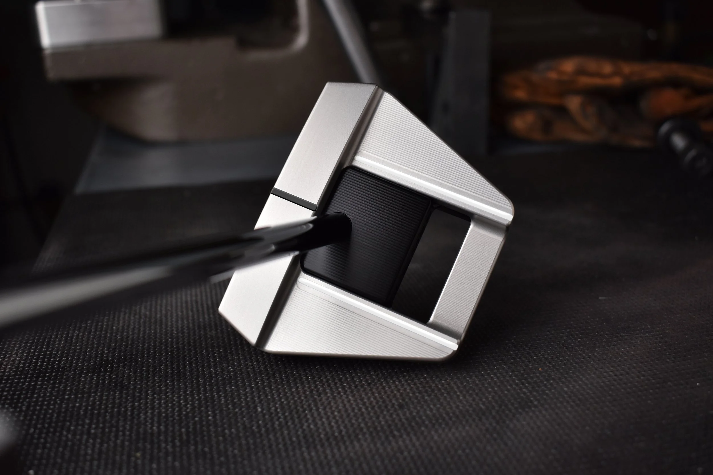 A precision machinist spike with a circular top and engraved 'JAMES' letter logo, mounted on a vice, with metal workpieces in the background.