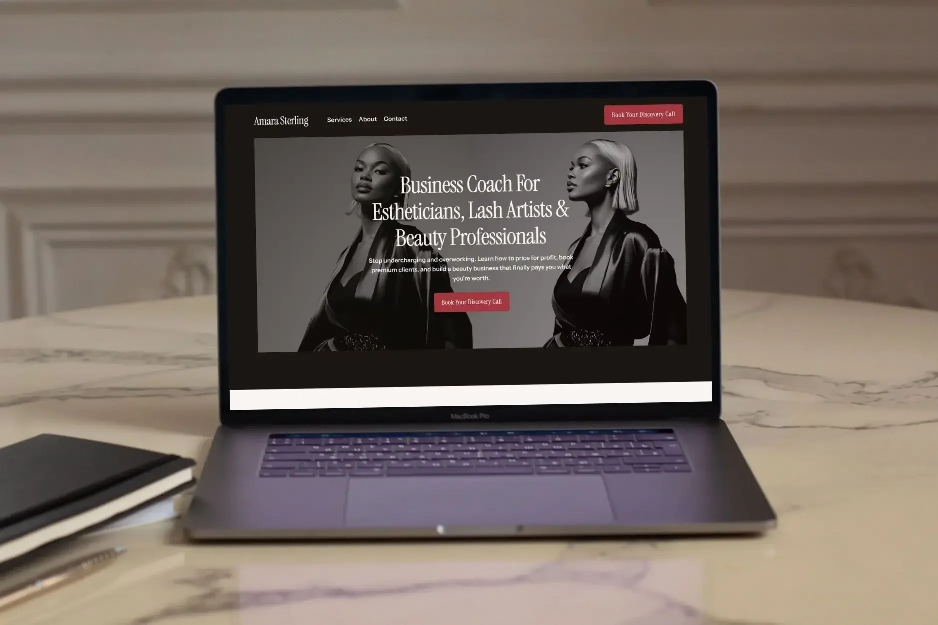 A laptop on a marble table displaying a dark-themed business coaching website for beauty professionals, featuring a black and white portrait of a woman.