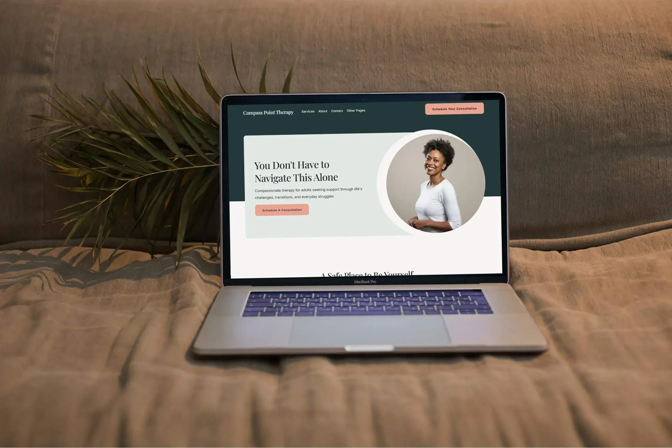 An open laptop on a cozy fabric surface showcasing a modern therapy website template that features a smiling woman in a circular frame.