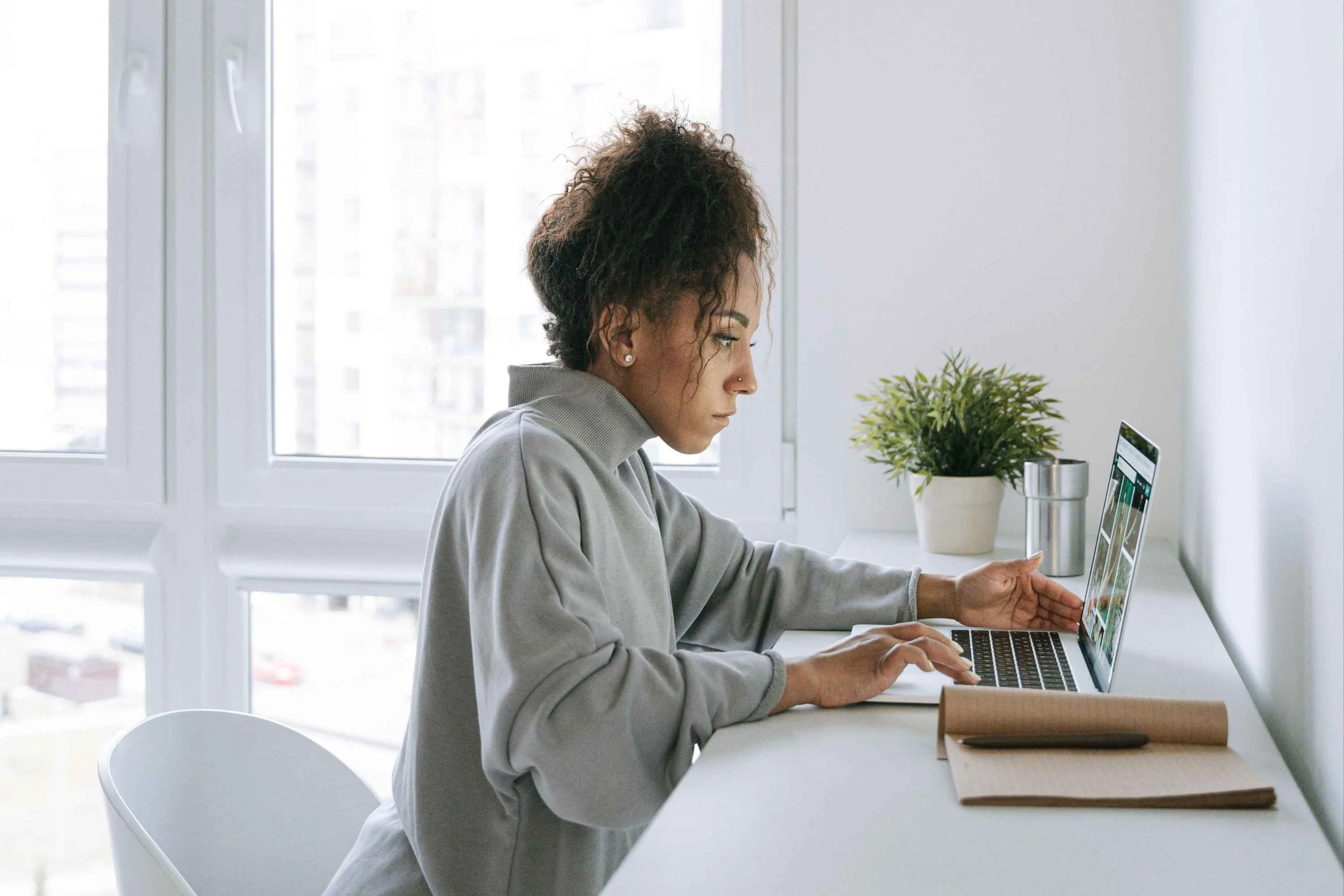 Woman sitting at a modern desk working on a laptop, focused on web design and customization.