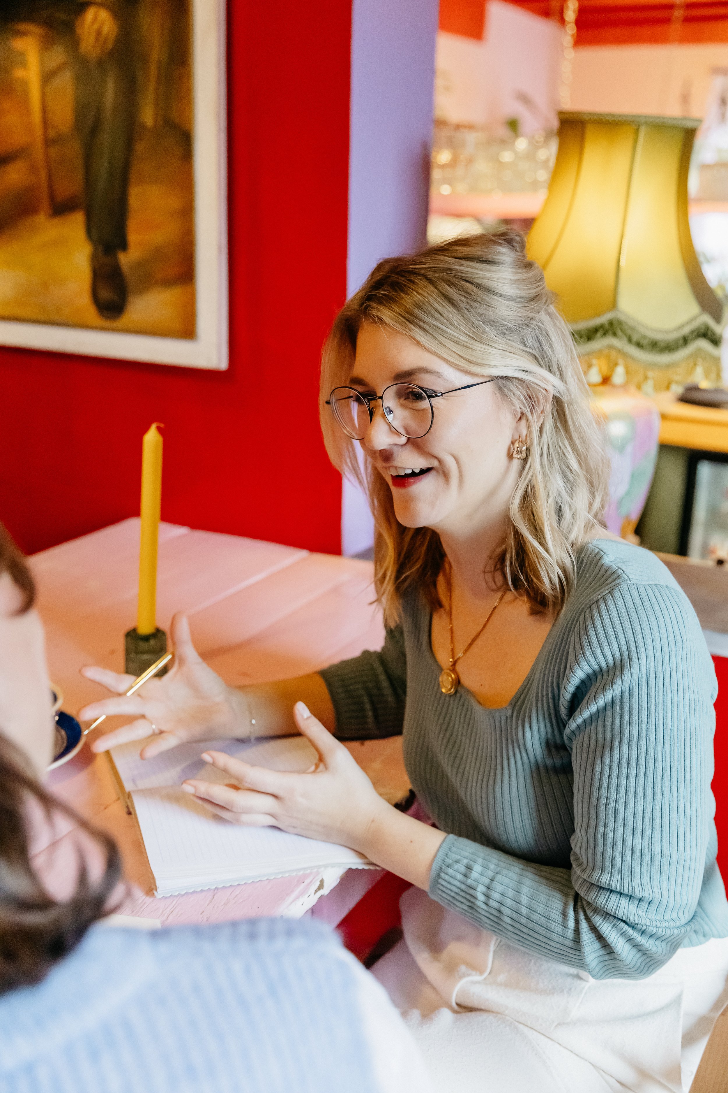 Kim die in een levendige kamer een gesprek voert, zit aan een tafel met een open notitieboekje en een pen.