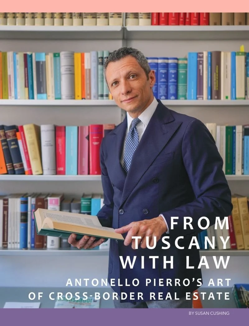 A man in a suit holding an open book, standing in front of bookshelves filled with colorful books.