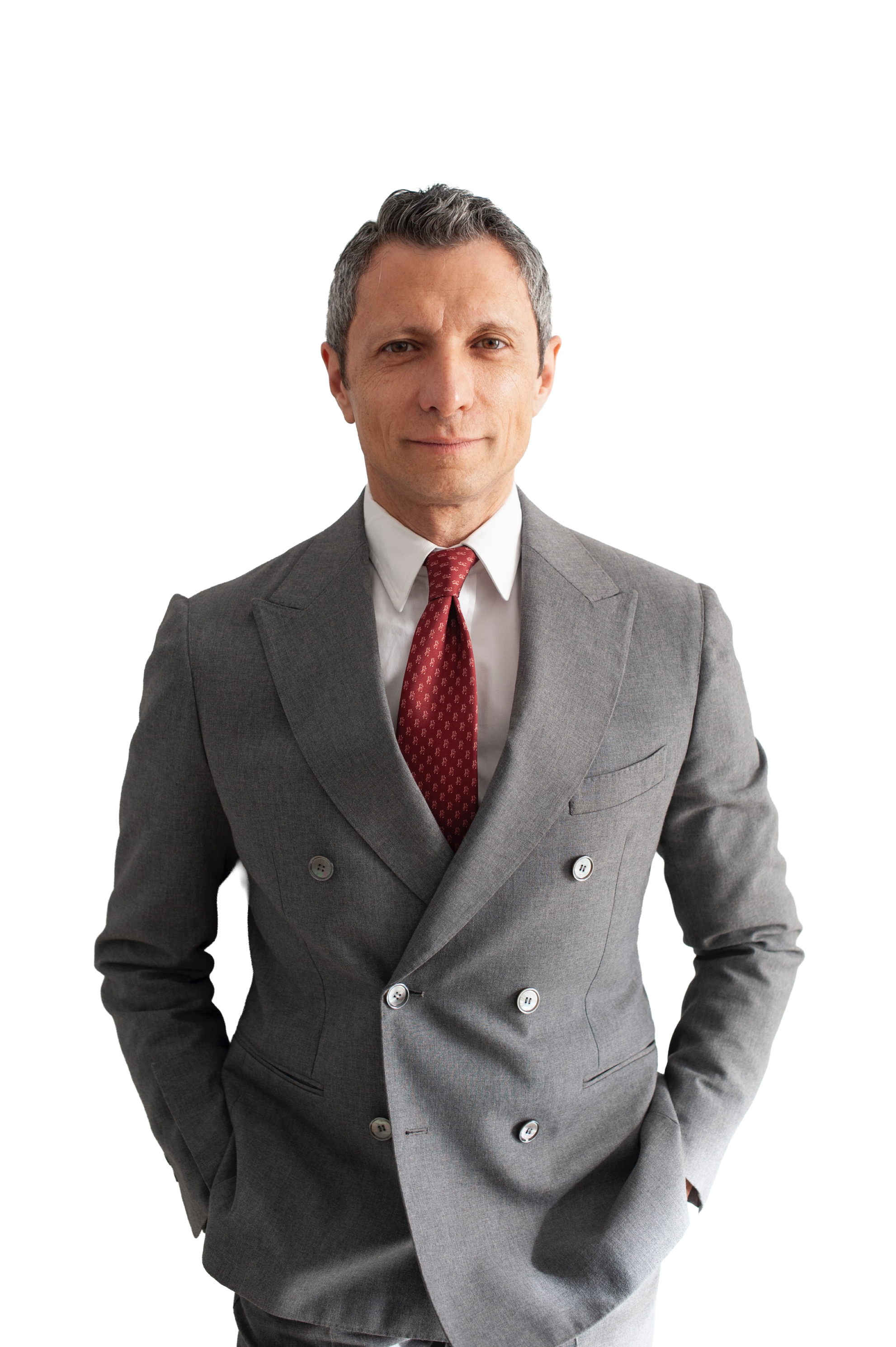 A middle-aged man in a gray double-breasted suit, white shirt, and red patterned tie, standing with hands in pockets and looking confidently at the camera.