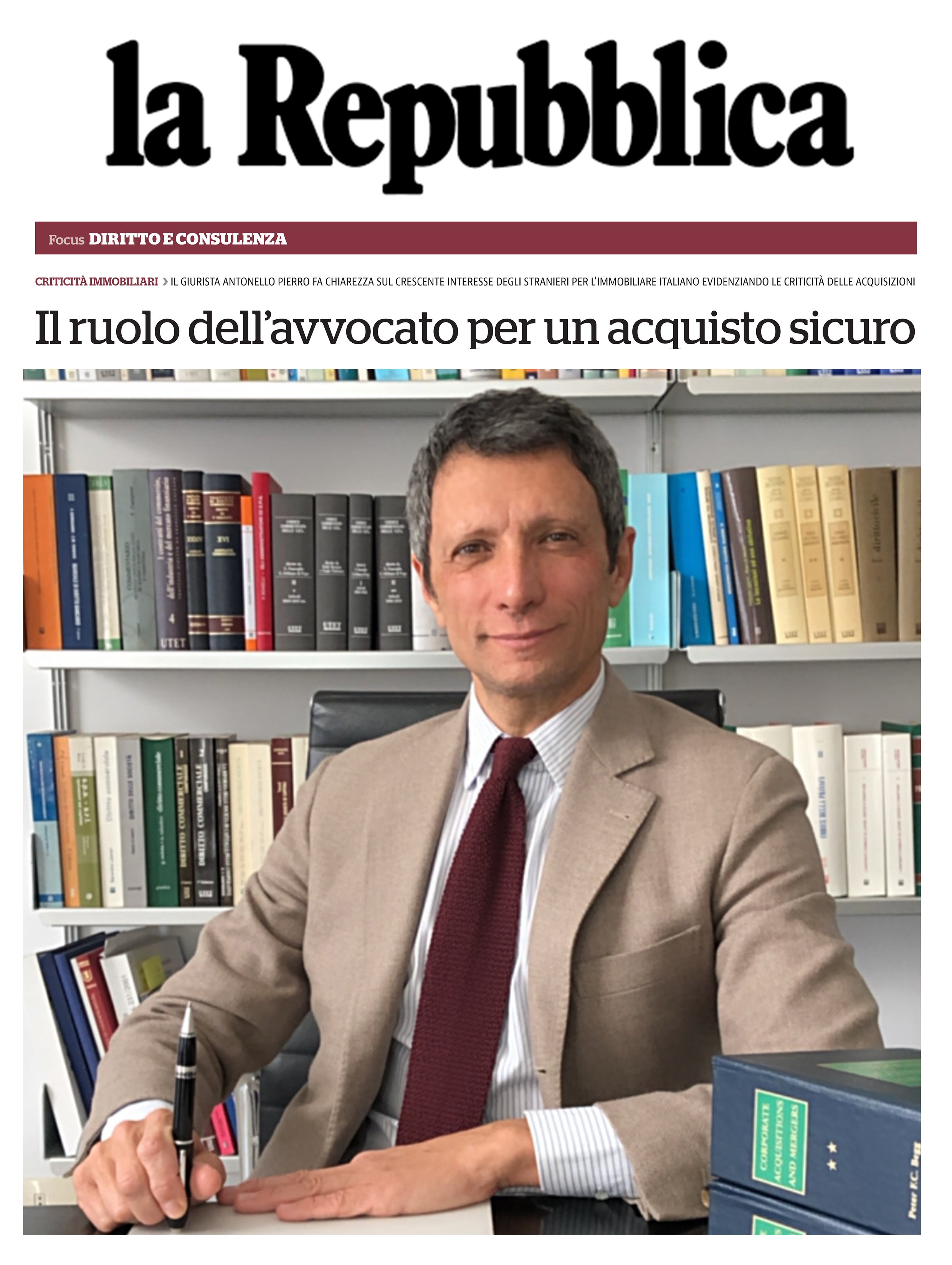 A man in a beige suit sitting at a desk in an office, surrounded by shelves filled with books, with a serious expression, holding a pen.
