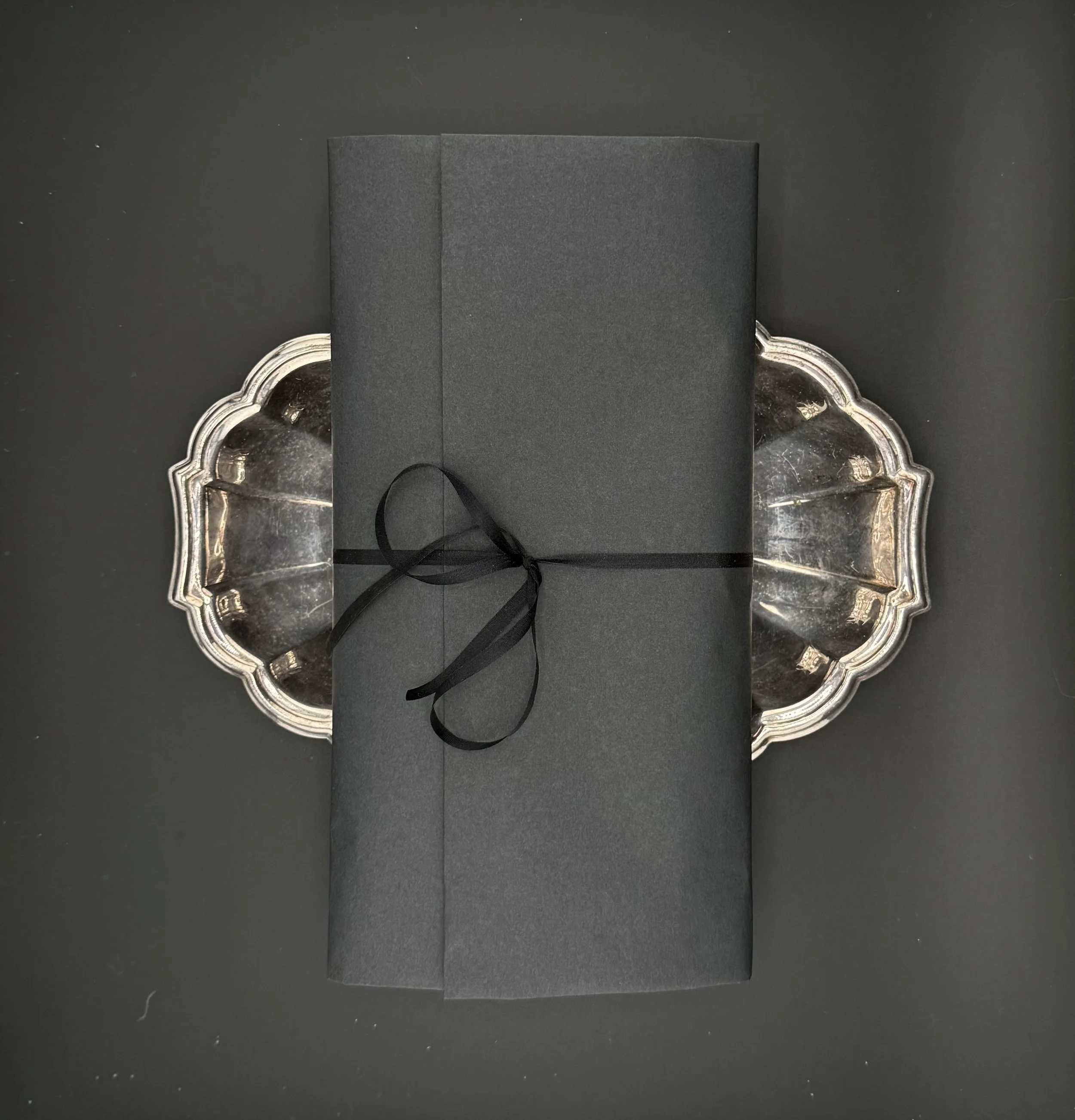 A black gift box tied with a black ribbon, placed on a silver tray on a black surface.