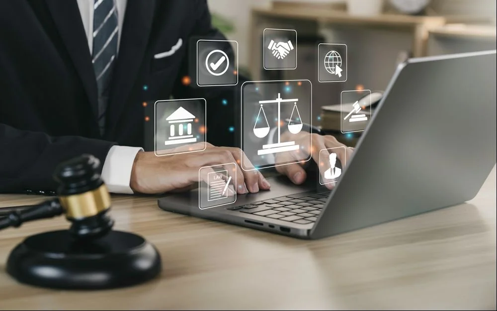Business person in suit using a laptop on a desk with legal and justice icons floating around, including a gavel, courthouse, scales, and law document.