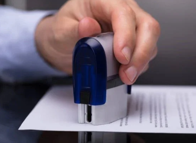 Person stamping a document with a blue and gray rubber stamp.