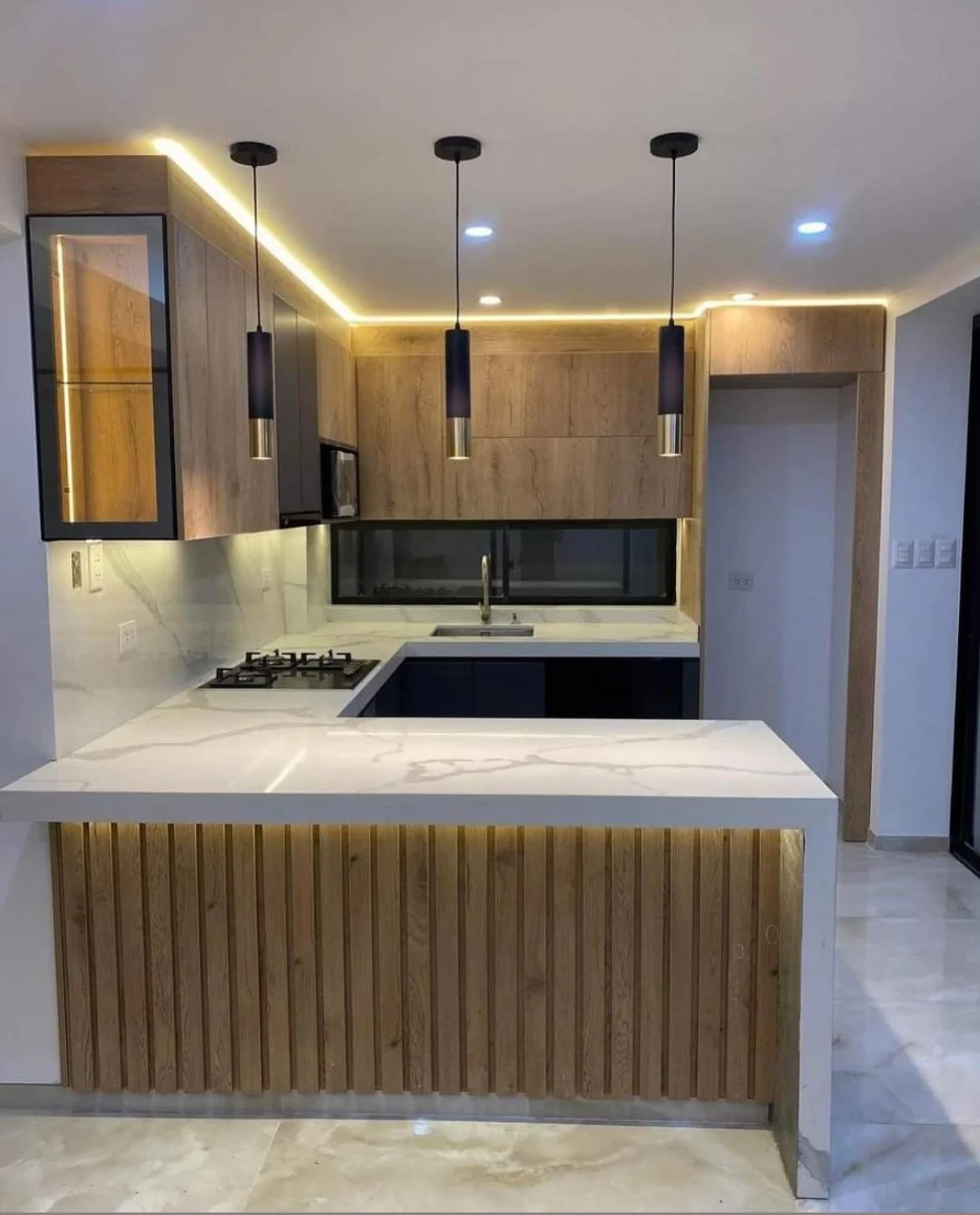 Modern kitchen with wooden cabinets, a white marble countertop, black pendant lights, and a window above the sink.