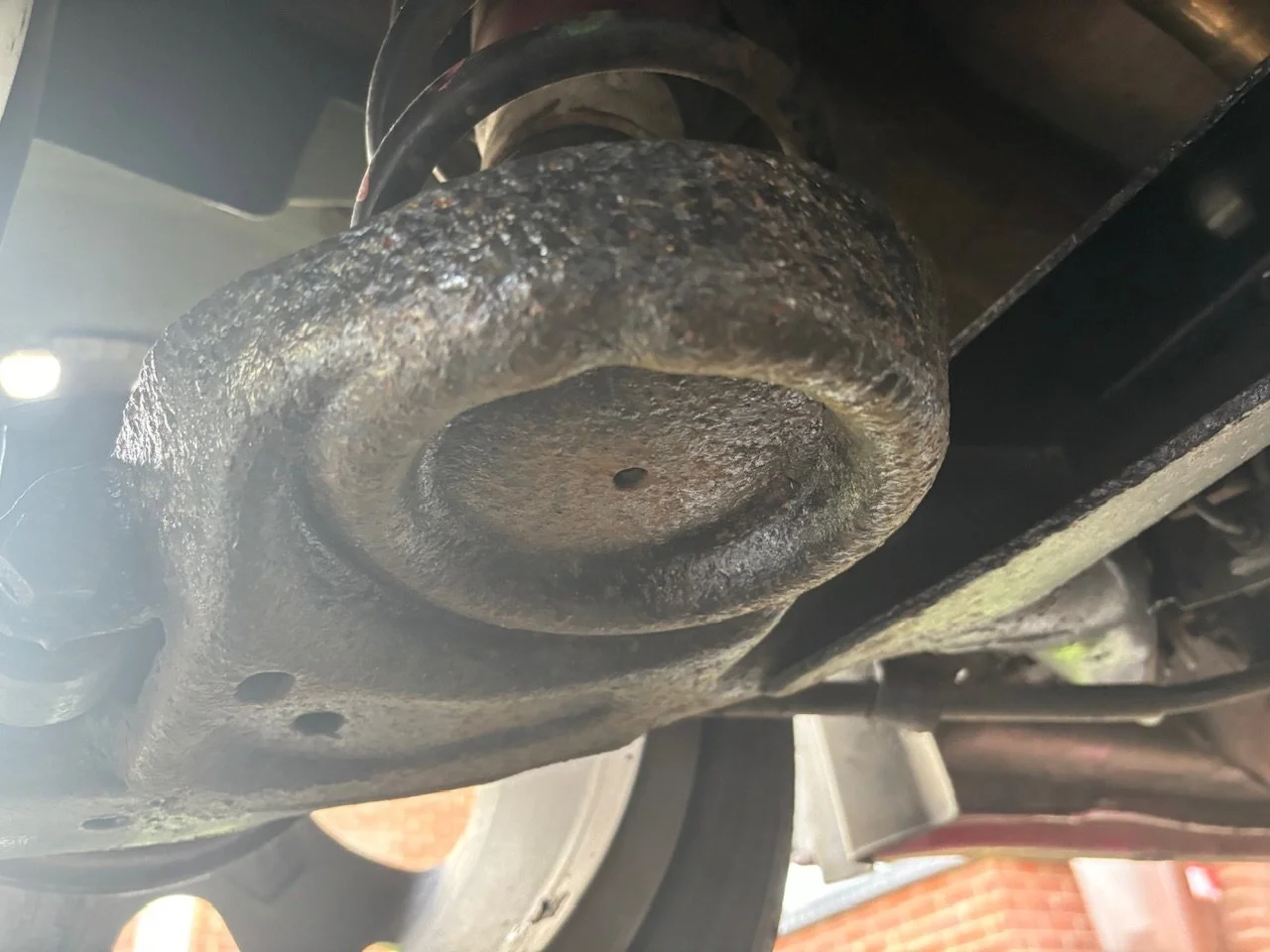 Close-up of a rusty, dirty part of a vehicle's undercarriage, possibly a suspension or axle component.