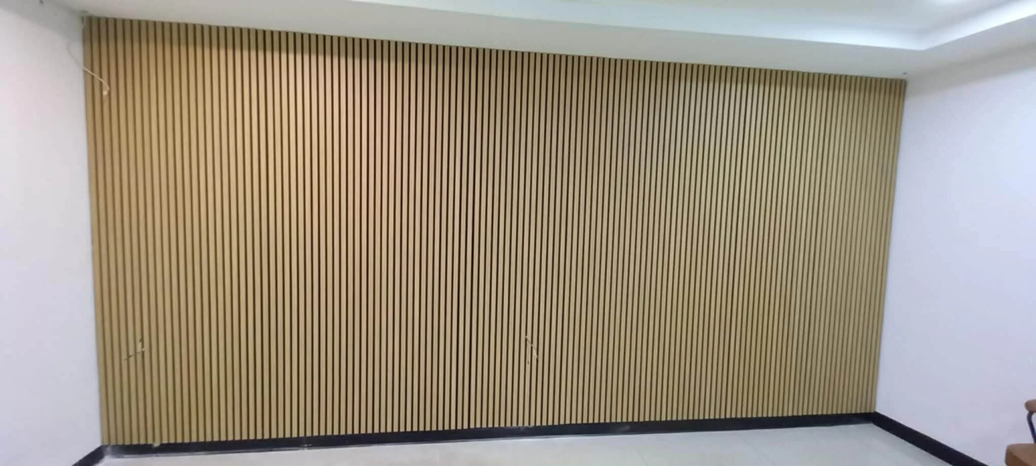 A large wooden slatted wall panel with vertical lines in a white-walled room.