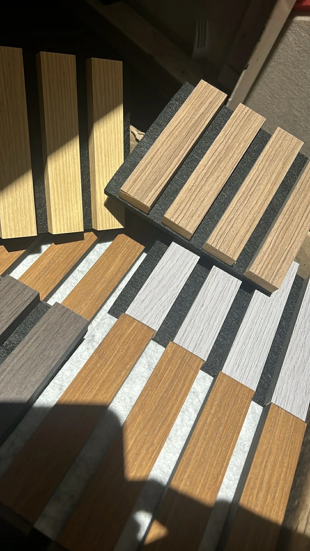 Assorted wood samples in different colors and grains laid out on black foam boards.