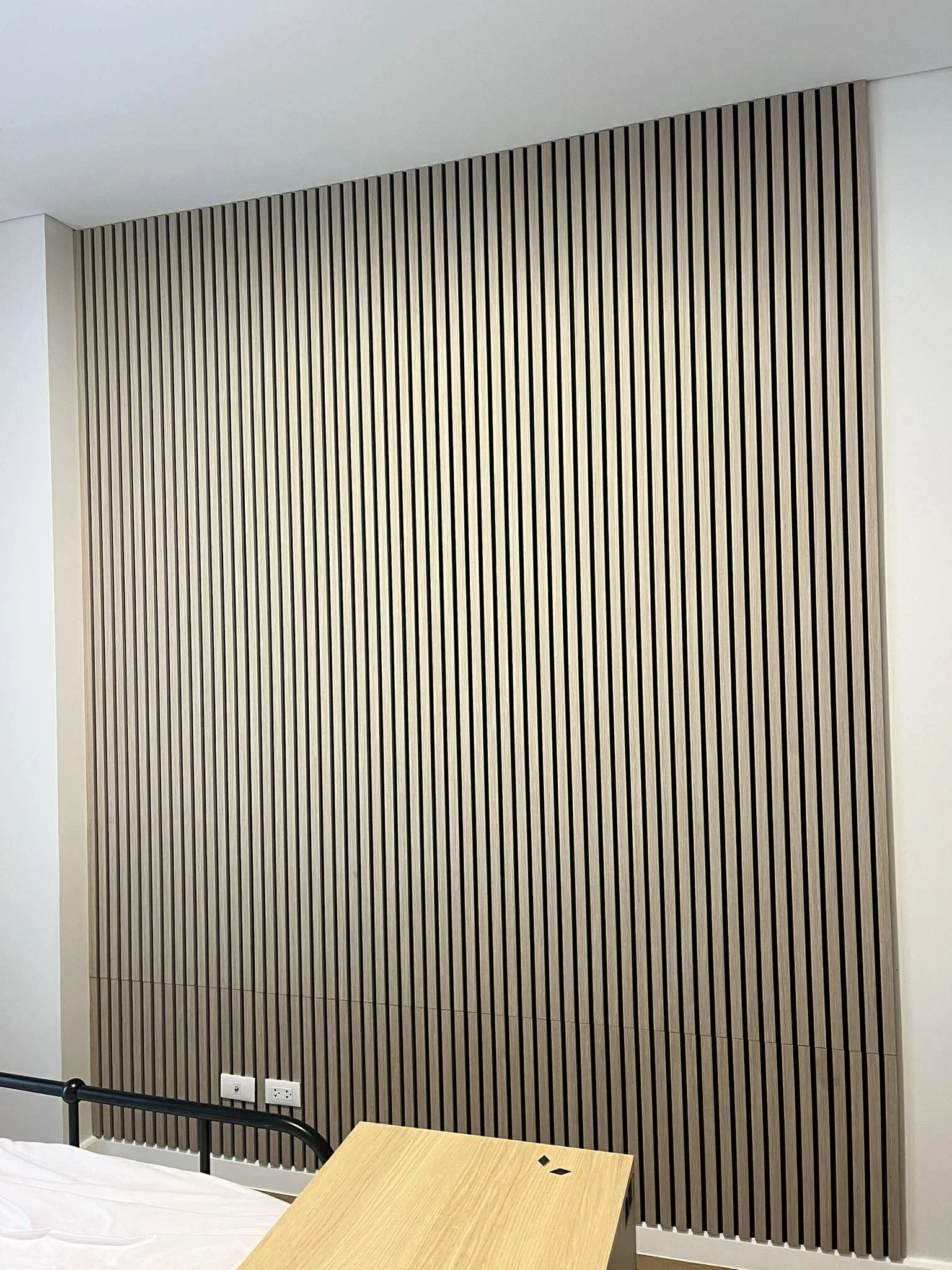 Wooden slat wall behind a bed and a small wooden table in a modern room.