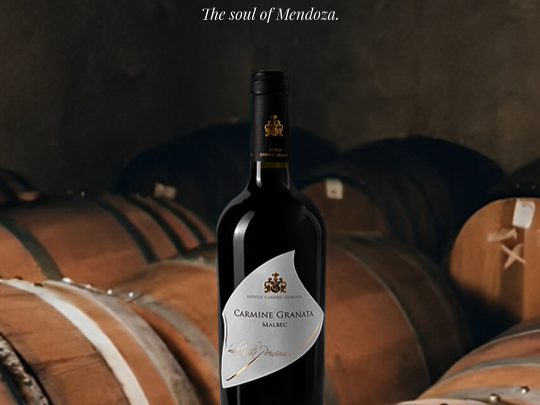 A bottle of Carmine Granata Malbec wine standing on a wine barrel in a cellar, with more barrels in the background. The text 'The soul of Mendoza.' is at the top of the image.