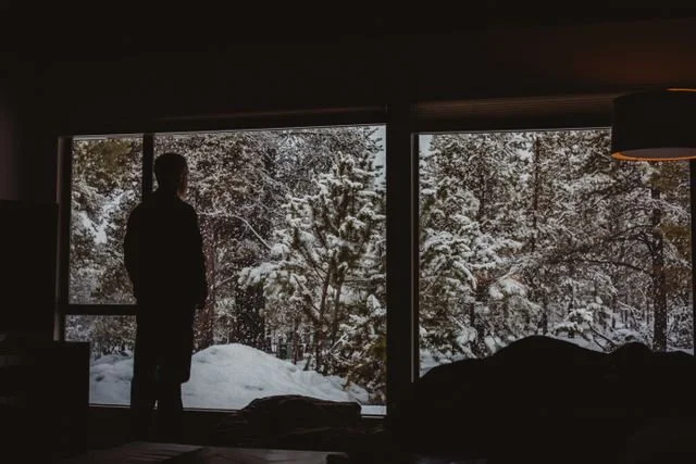 man looking out of window at snow