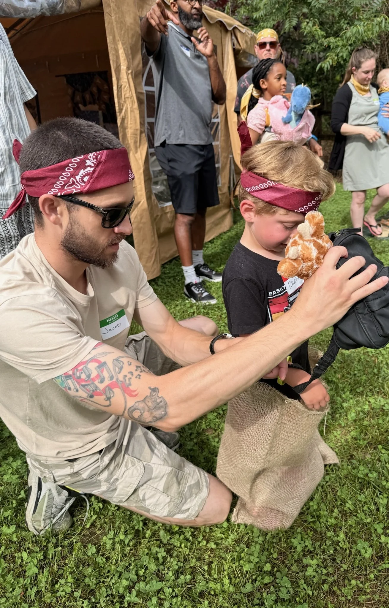 A miniature paper campfire, tent, and campfire with pinecones and stones on a green surface, with a blurred teddy bear in the background.