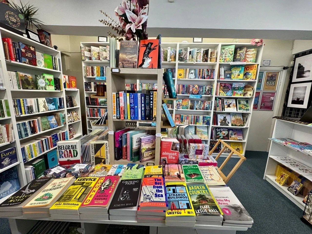 Bookshelves filled with books in a bookstore or library with a table displaying various book titles in the foreground.
