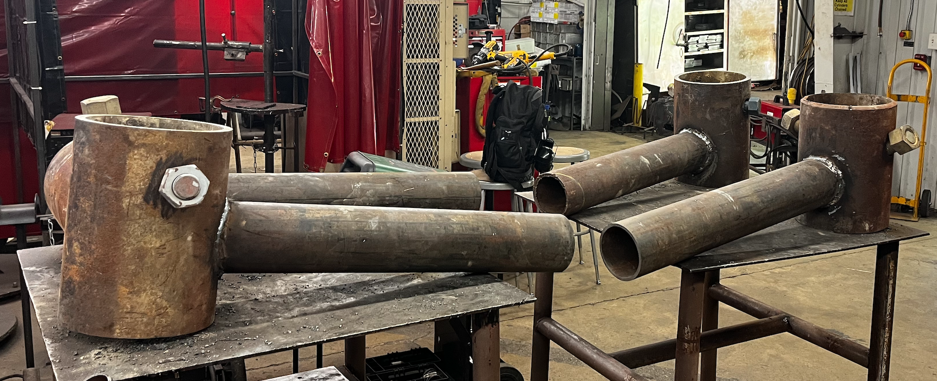 Large welded metal pipe components with flanges in an industrial workshop setting.